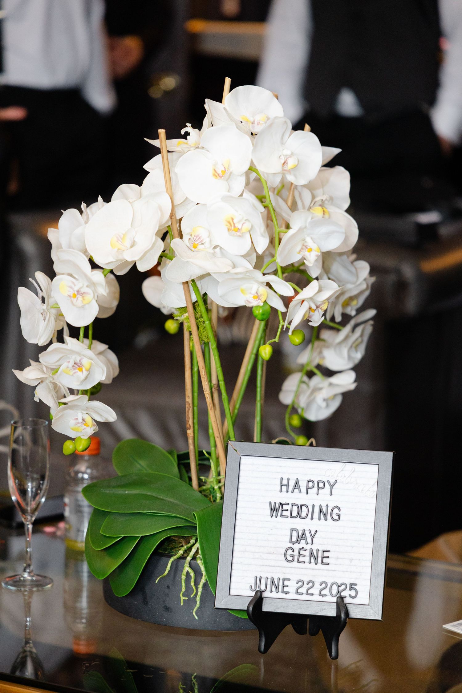 White orchid centerpieces with wedding date cards displayed on tables at an elegant reception celebration.