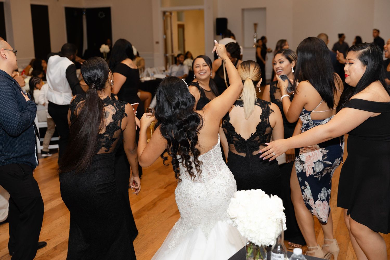 Wedding party guests dance together on a wooden dance floor during a lively reception celebration.
