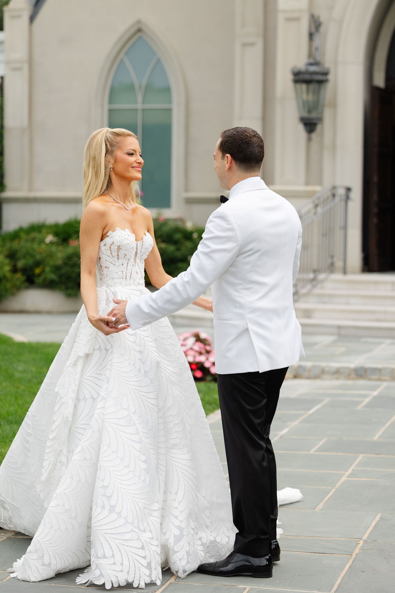 Bride and groom dance together on stone patio outside elegant church with stained glass windows in background.