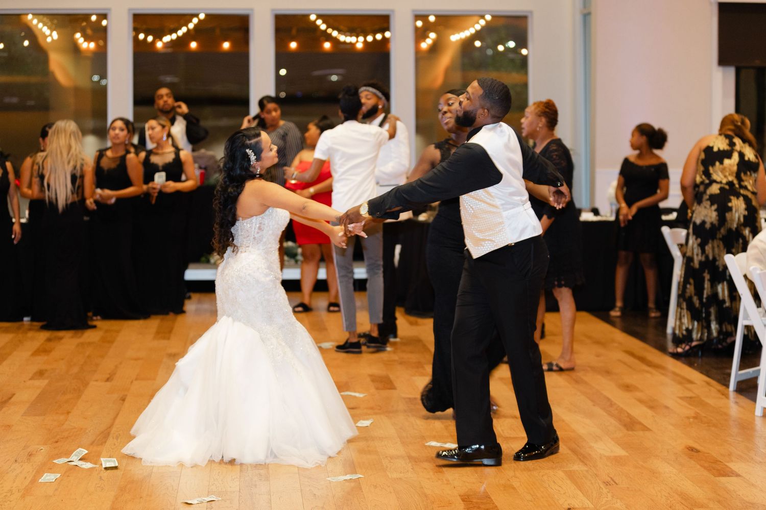 Dancers in formal attire move gracefully across a wooden dance floor at an elegant reception with string lights overhead.