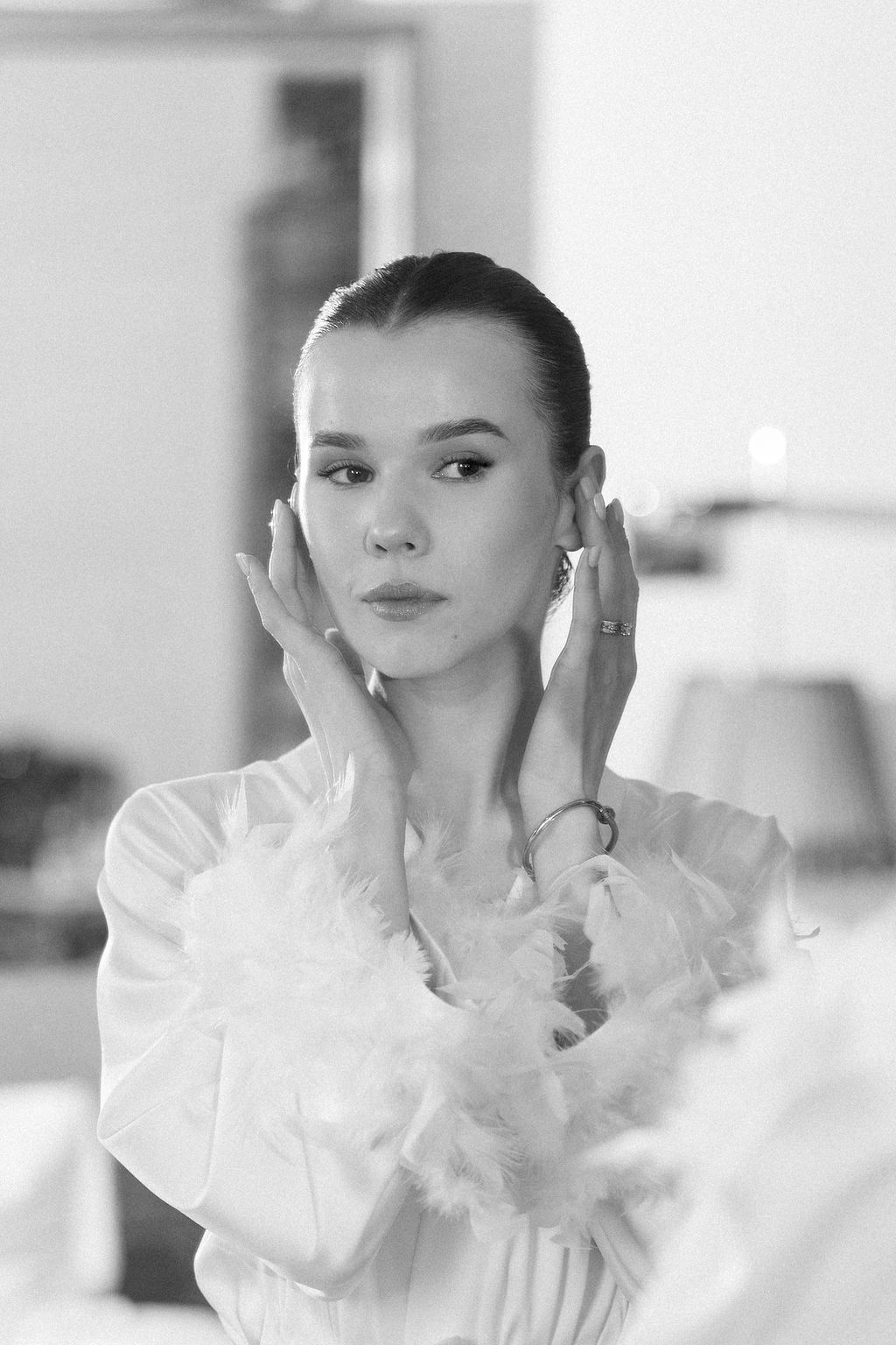 Black and white portrait of someone in a delicate white ruffled dress with hands near face.