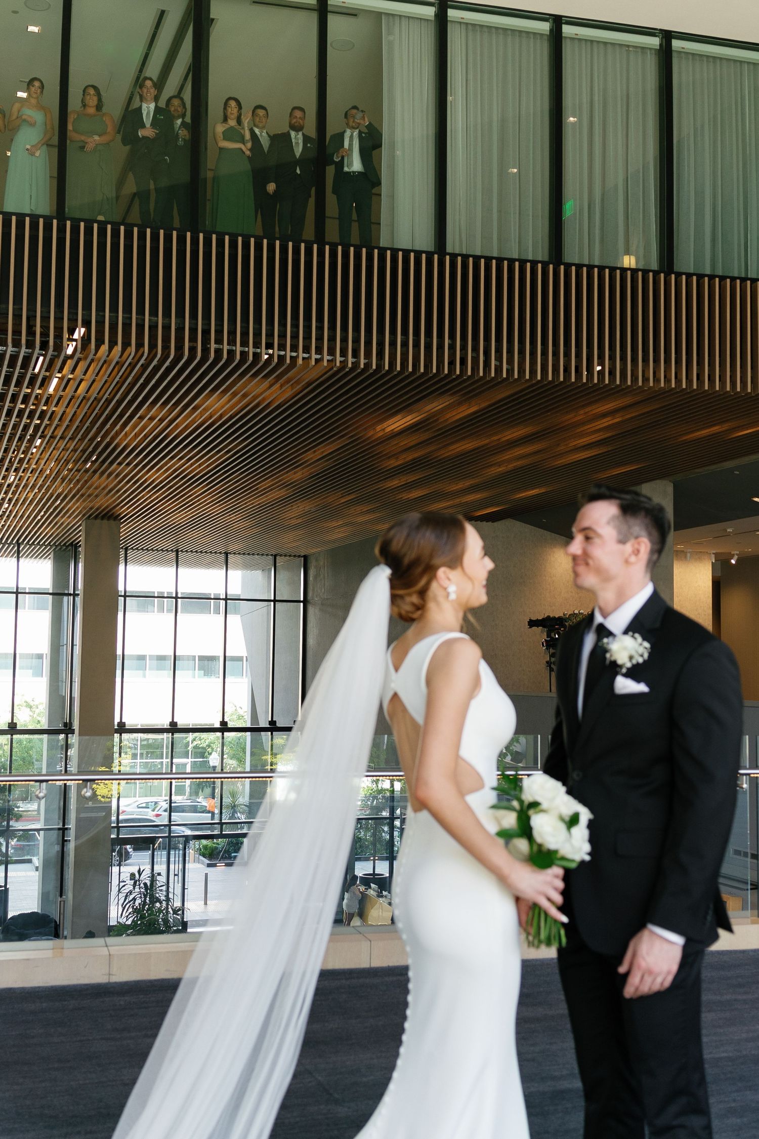 A couple shares a romantic moment at their wedding ceremony while guests watch from a balcony above.