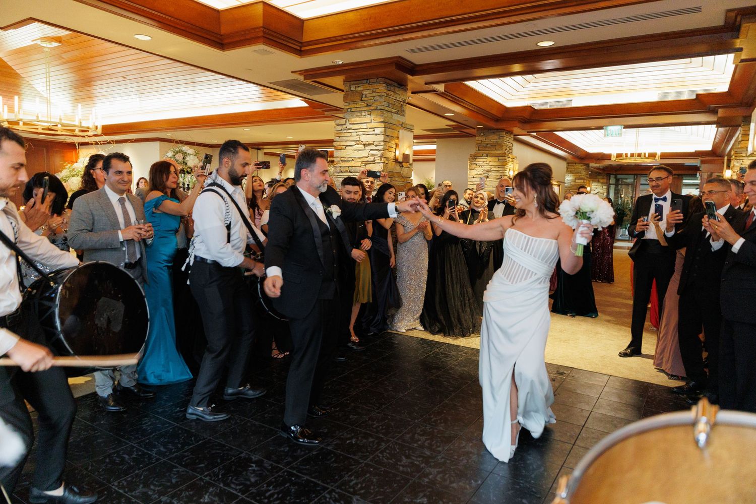 People raise their hands in celebration during a lively indoor gathering in a room with wooden ceiling beams.
