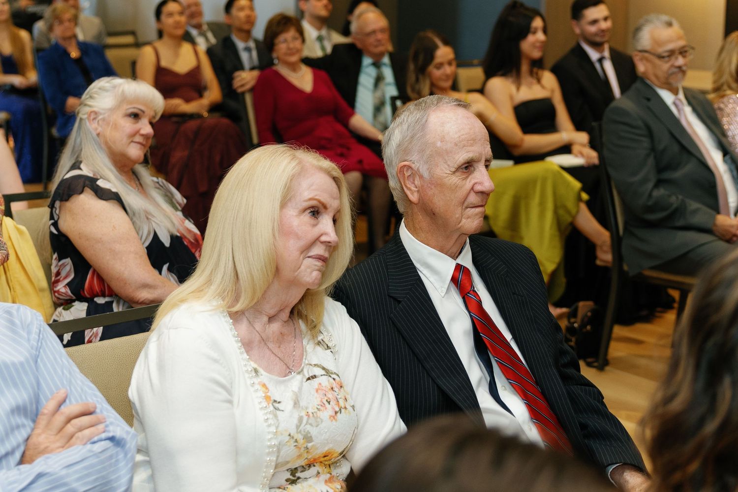 Wedding guests seated in rows at a formal ceremony watching attentively in an indoor venue.