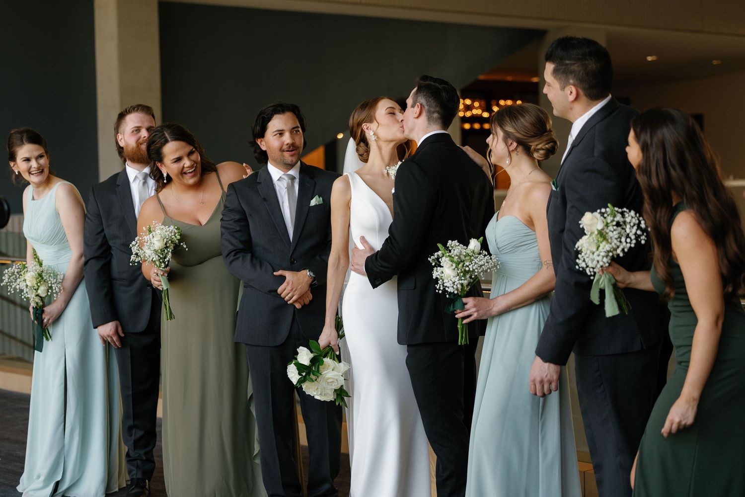 Wedding party members in light blue bridesmaid dresses and dark suits gather for formal photos.