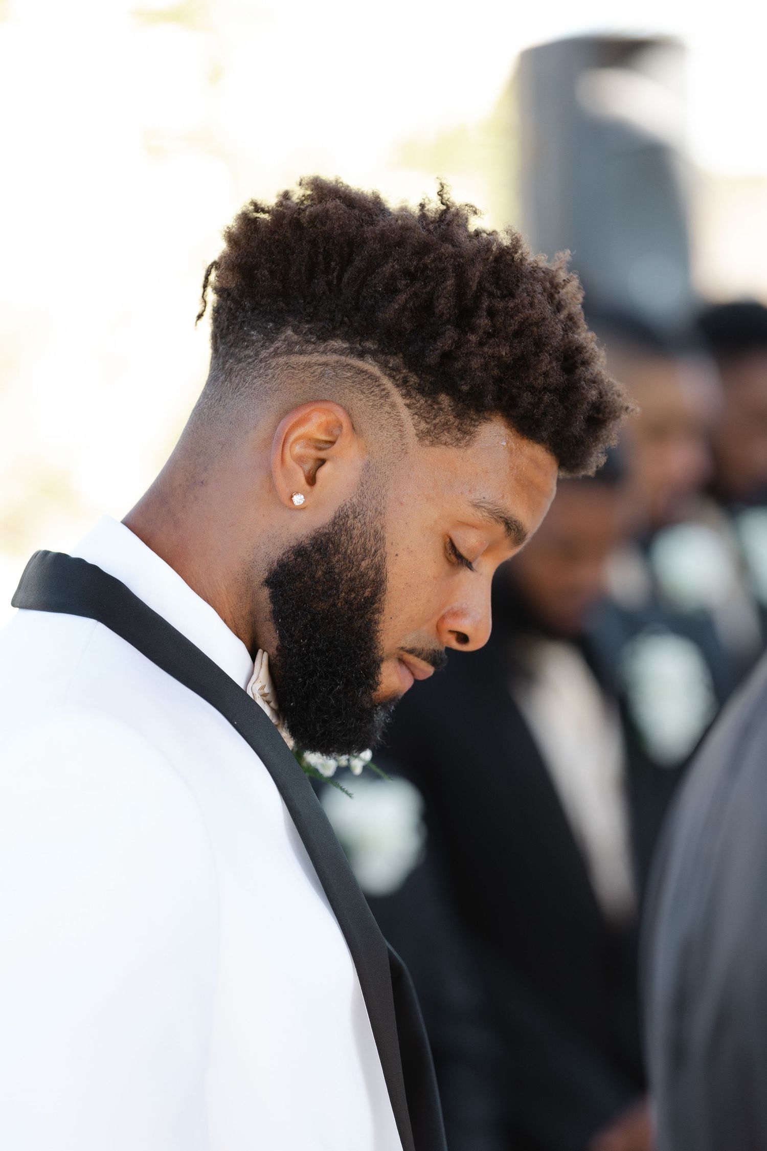 A person in a white tuxedo jacket and black bow tie smiles while looking down during a formal event.