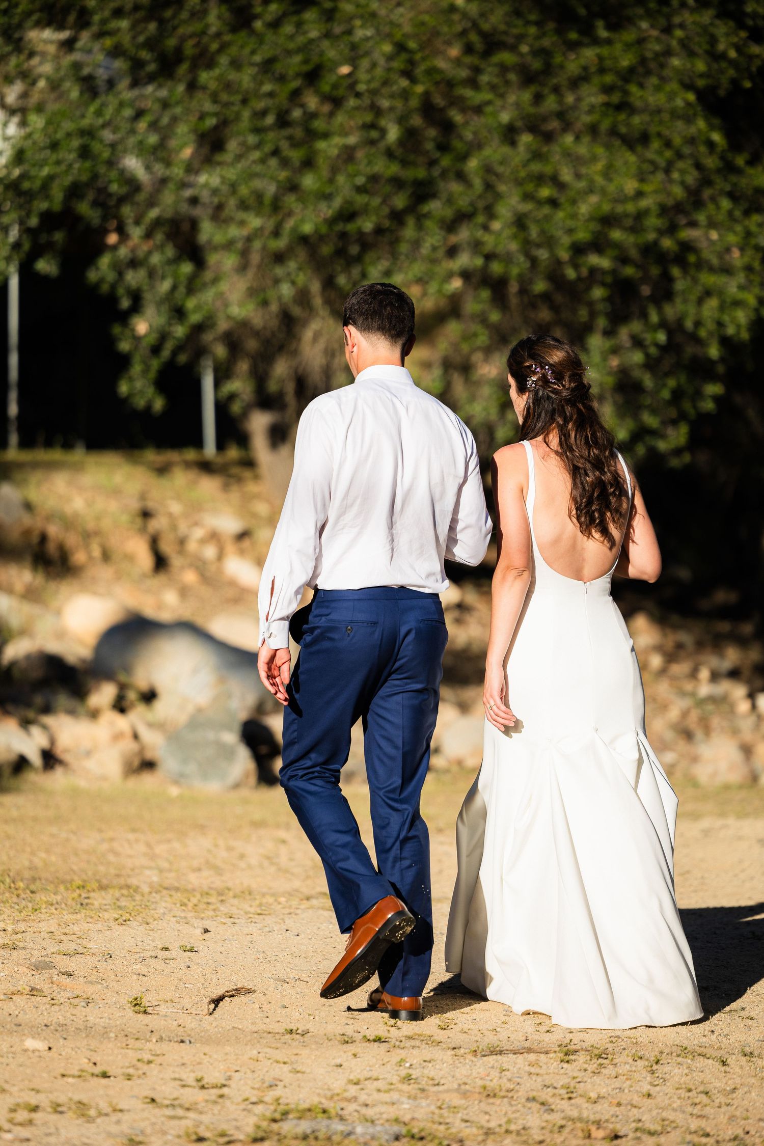 A couple in wedding attire walks together on a sandy beach path during a sunset photo session.