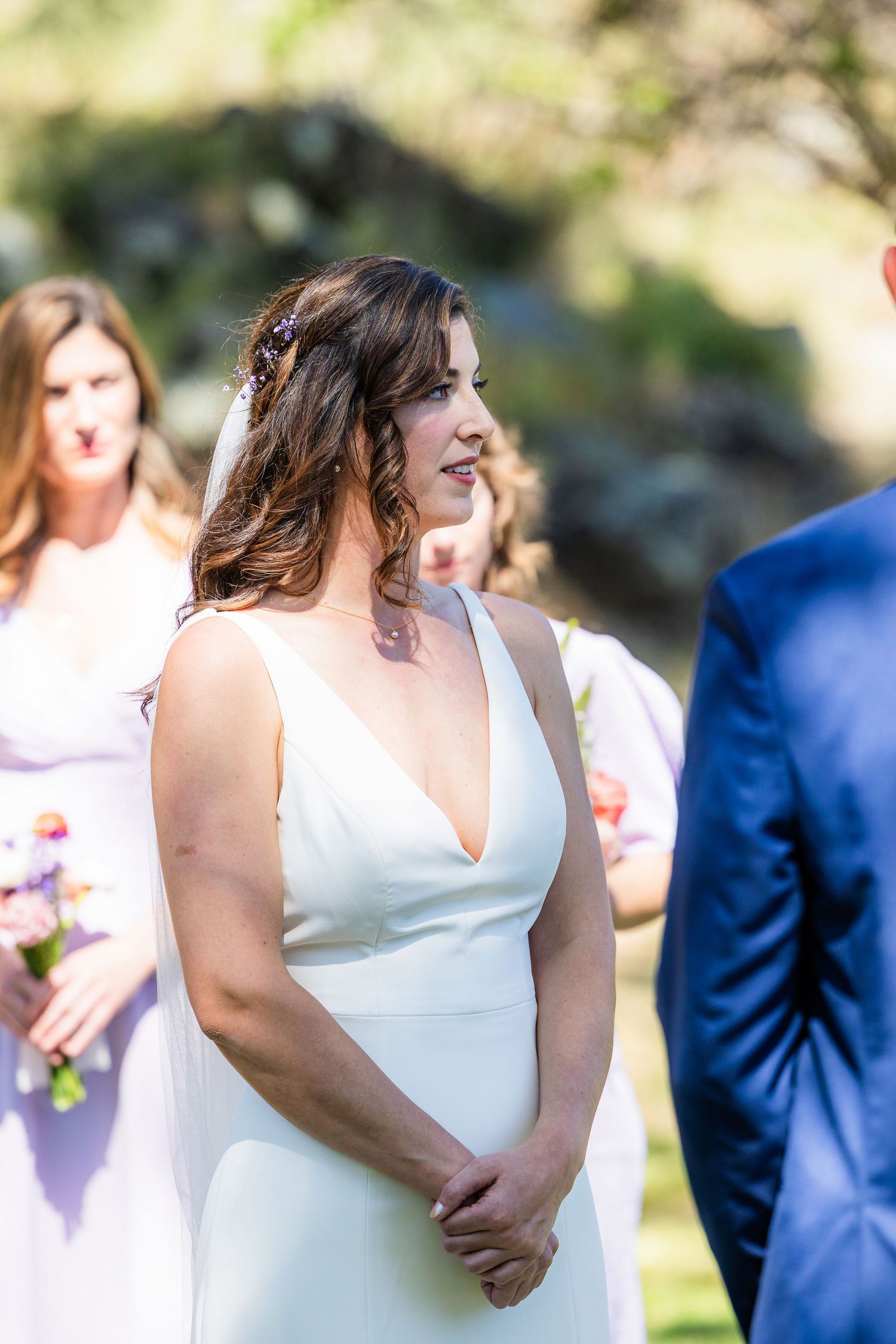 A bride in a sleek white V-neck wedding dress stands at the altar during an outdoor ceremony.