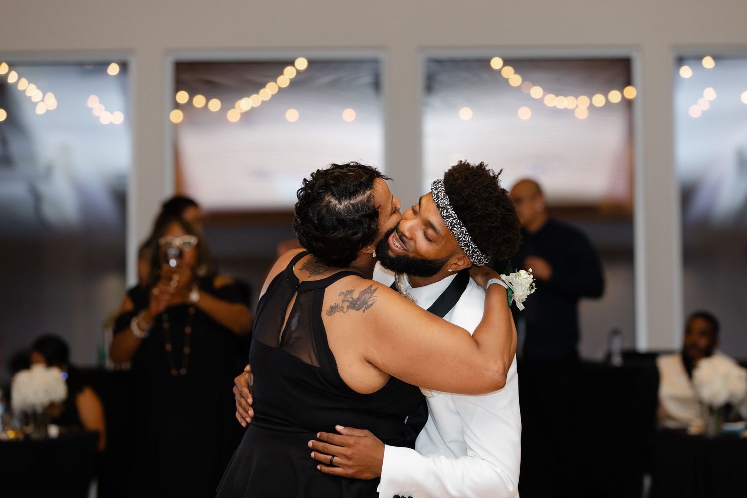 A couple shares a romantic dance moment at a wedding reception with string lights glowing in the background.