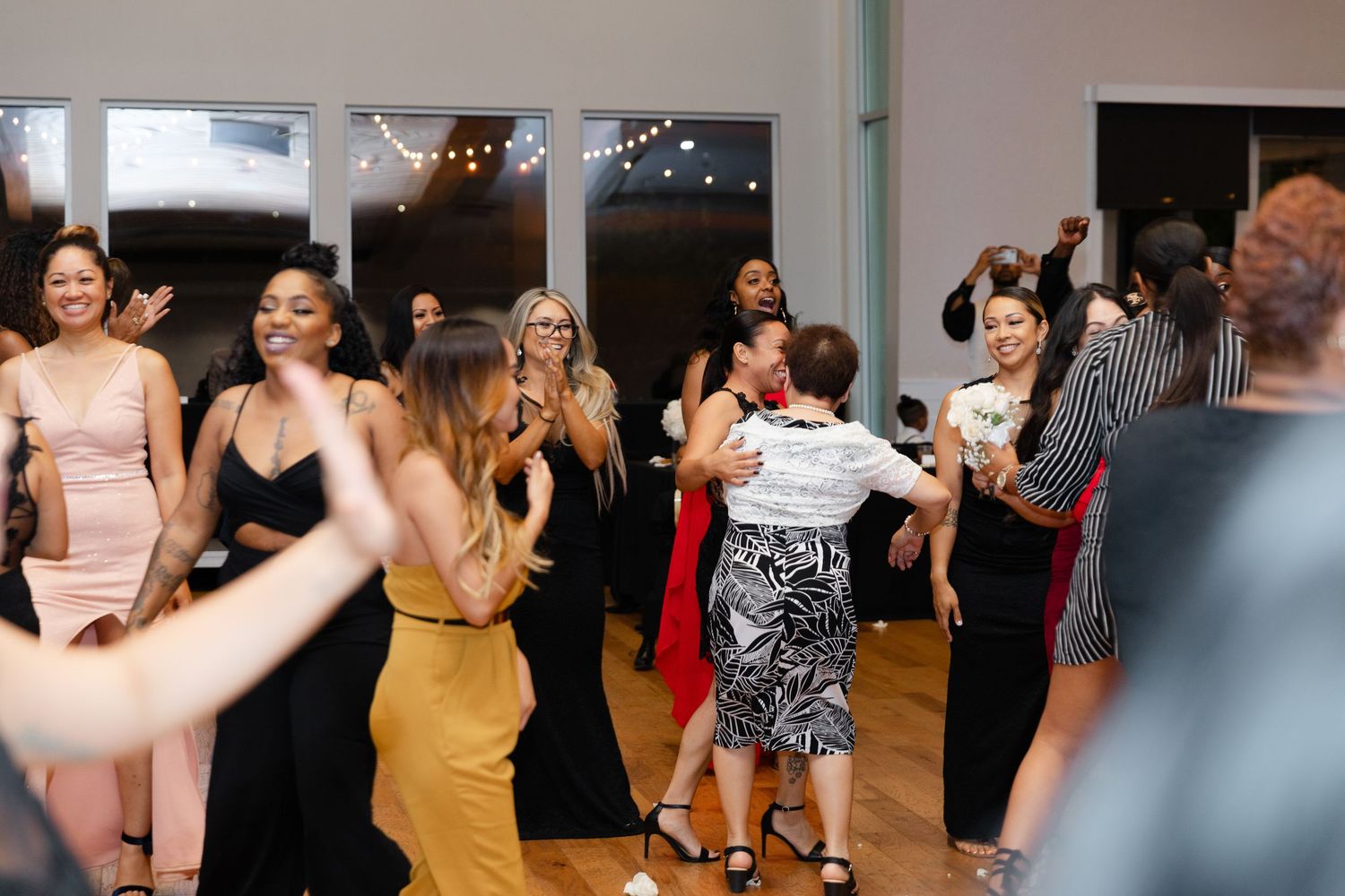 A group of people dancing and celebrating together at a wedding reception with string lights in the background.
