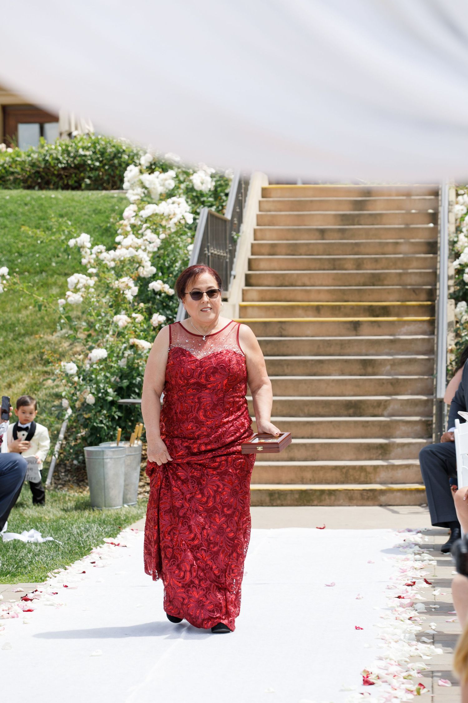 Someone in a red floral dress descends stone steps outdoors surrounded by white flowering bushes.
