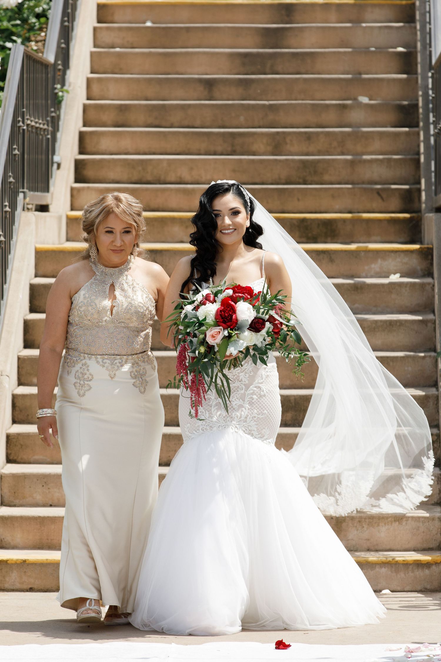 Wedding party members in white dresses pose together on rustic wooden steps with red and white floral bouquets.