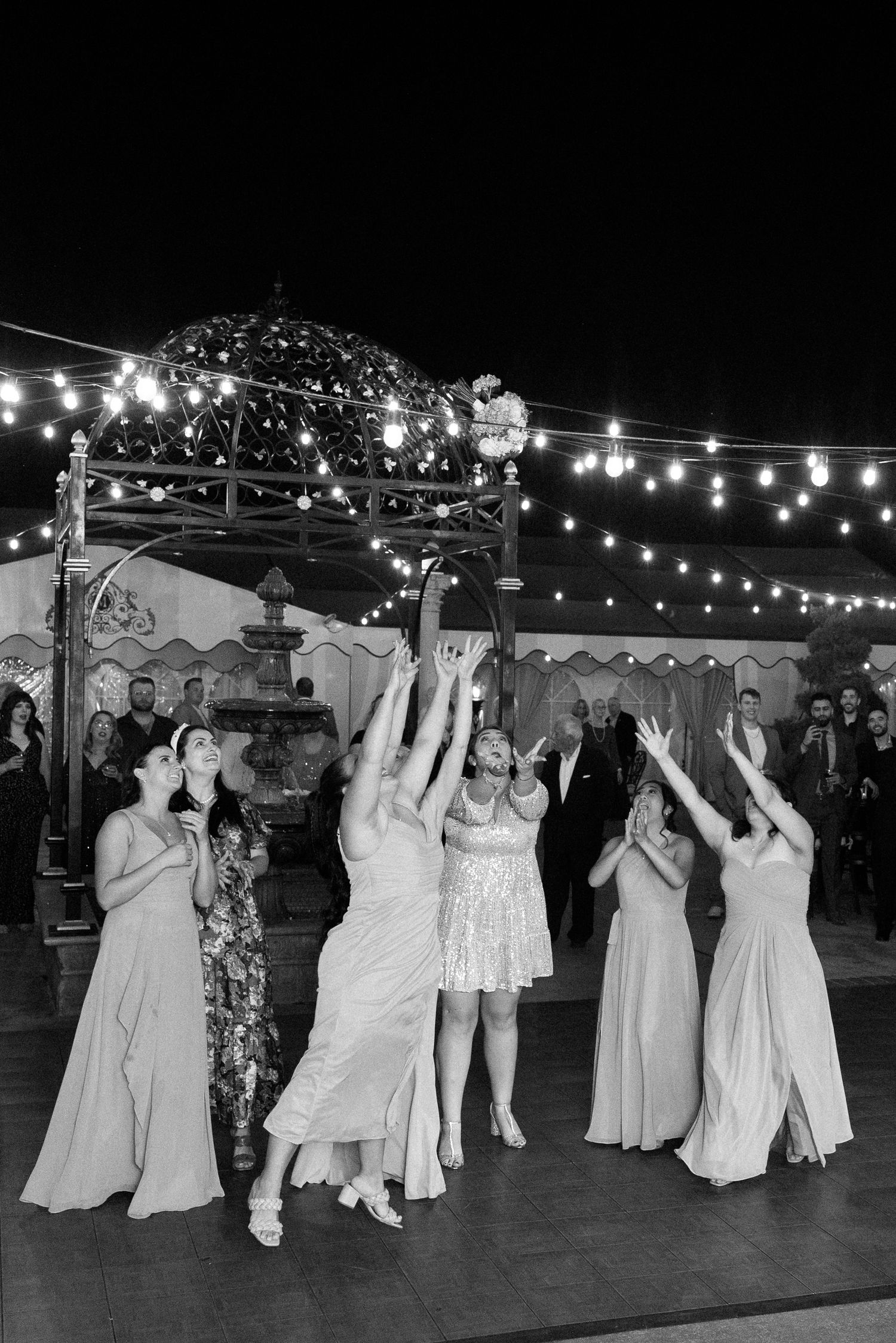 Wedding reception dance floor under string lights with guests dancing in formal attire.