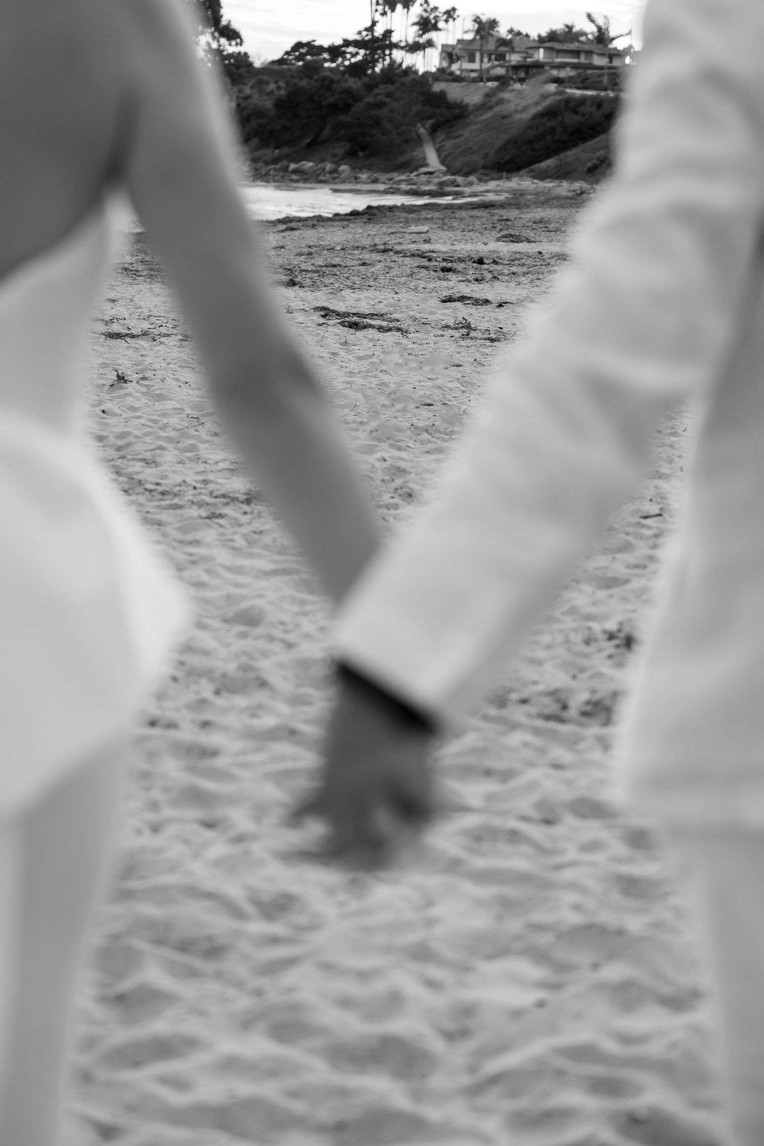 Black and white close-up of joined hands walking on sandy beach.