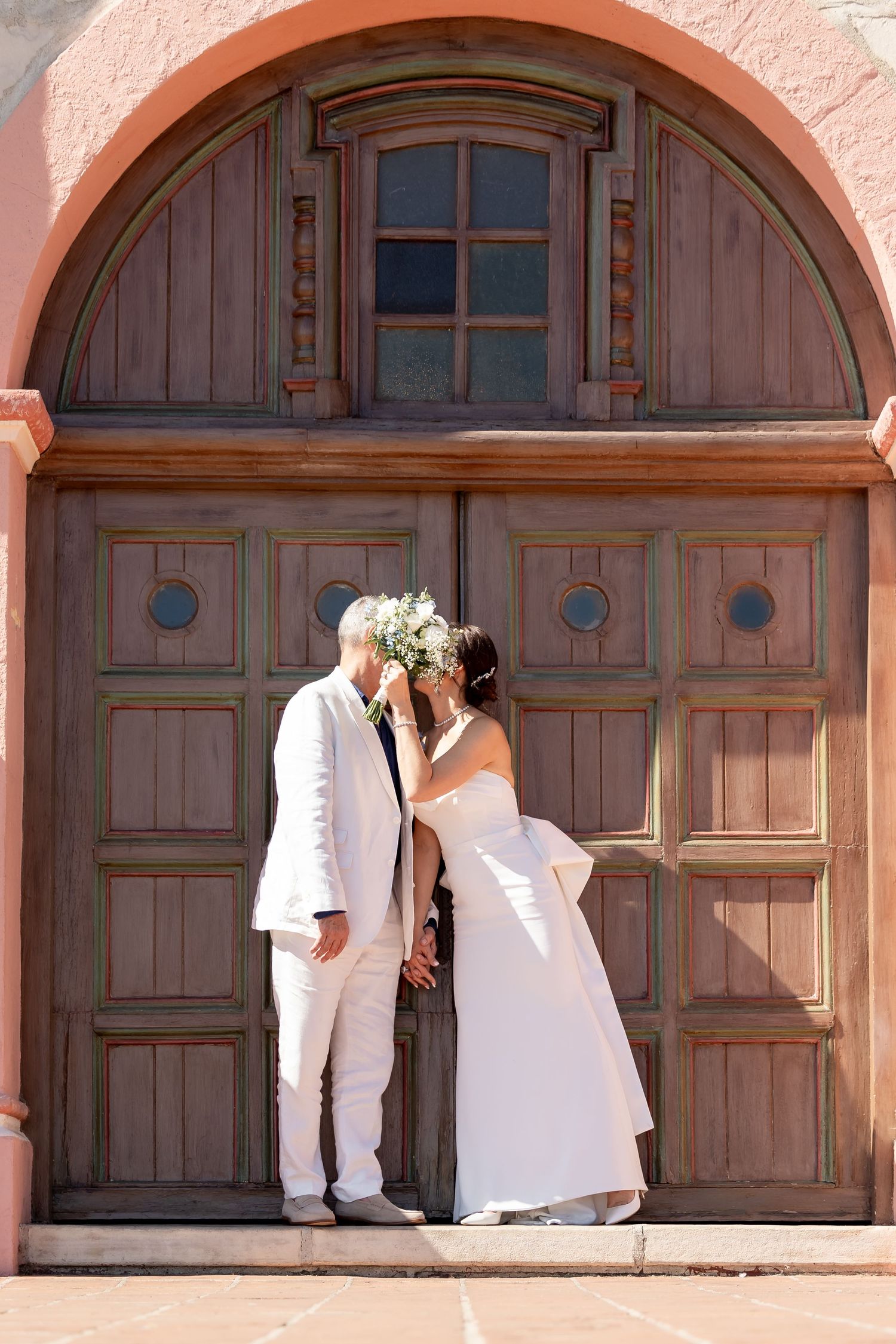 A romantic wedding photo series under pink archways with wooden doors showing intimate moments between newlyweds.