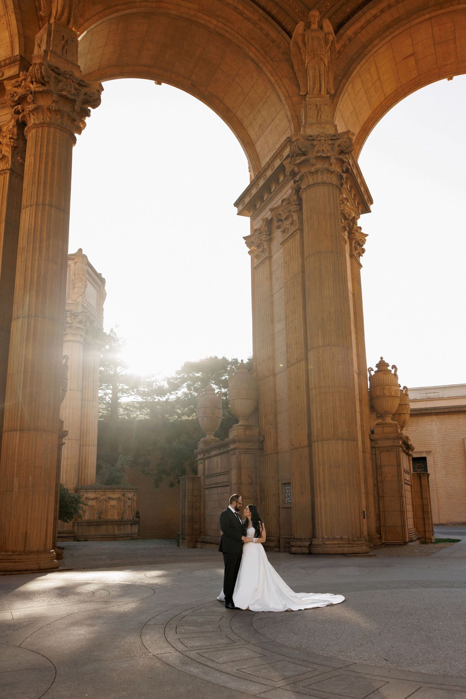 Romantic wedding portraits under grand stone archways with dramatic sunlight.