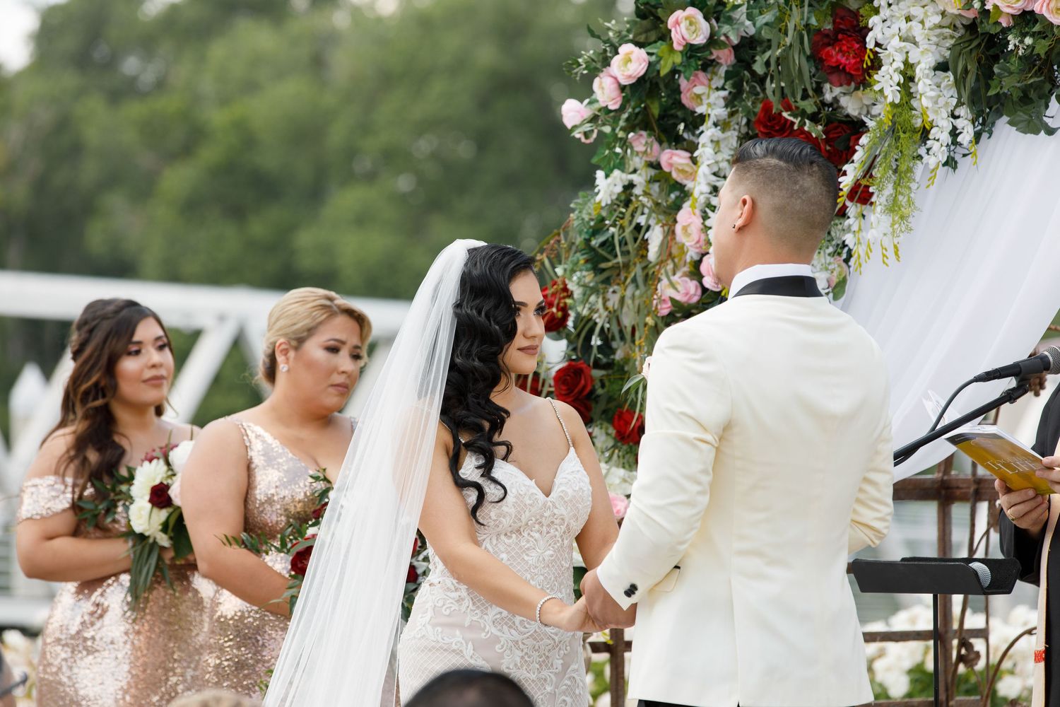 A wedding ceremony setup outdoors with white chairs, floral arrangements, and a decorative arch with red and white flowers.