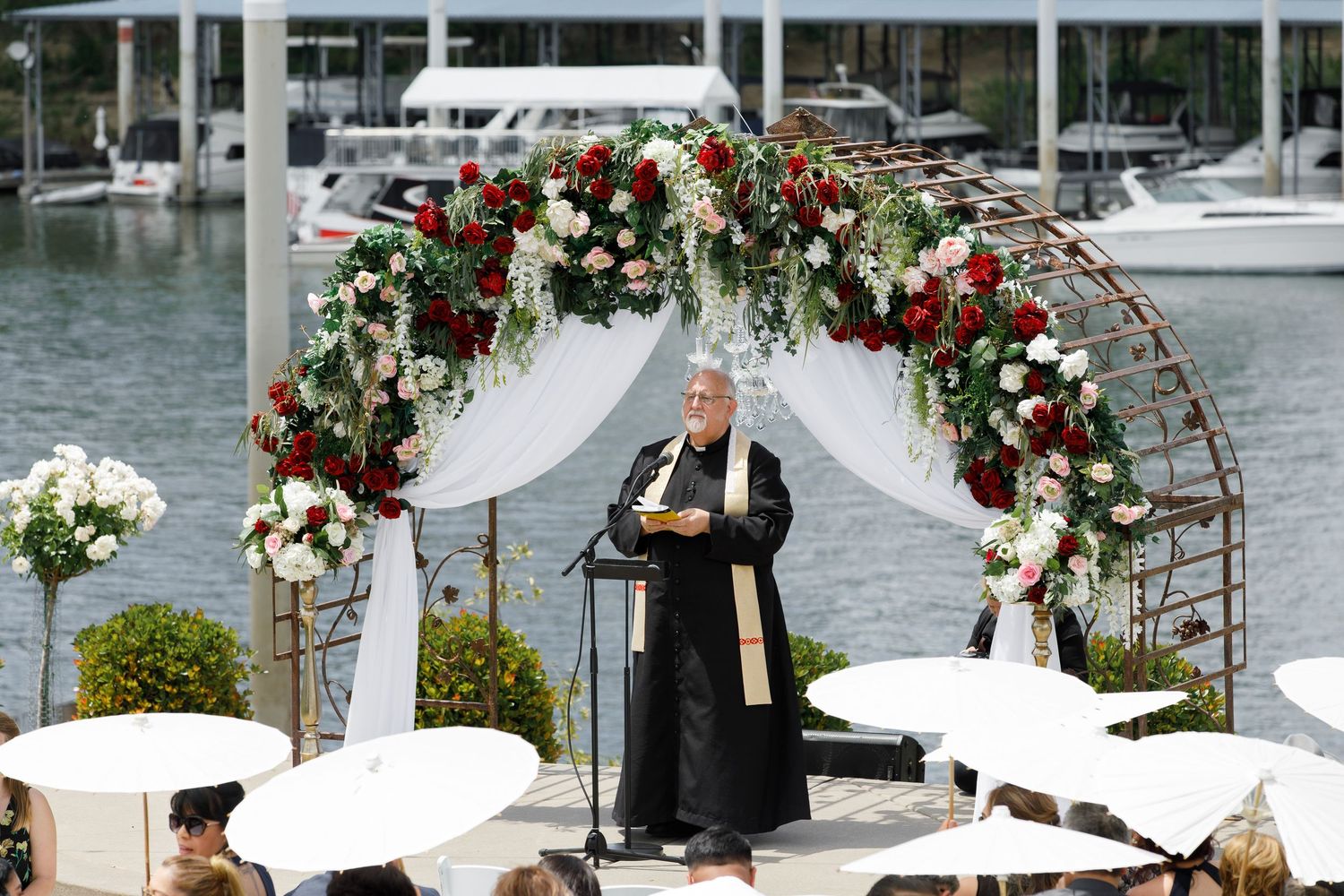 Elegant wedding ceremony setup on a dock with white chairs and floral arch overlooking a marina.