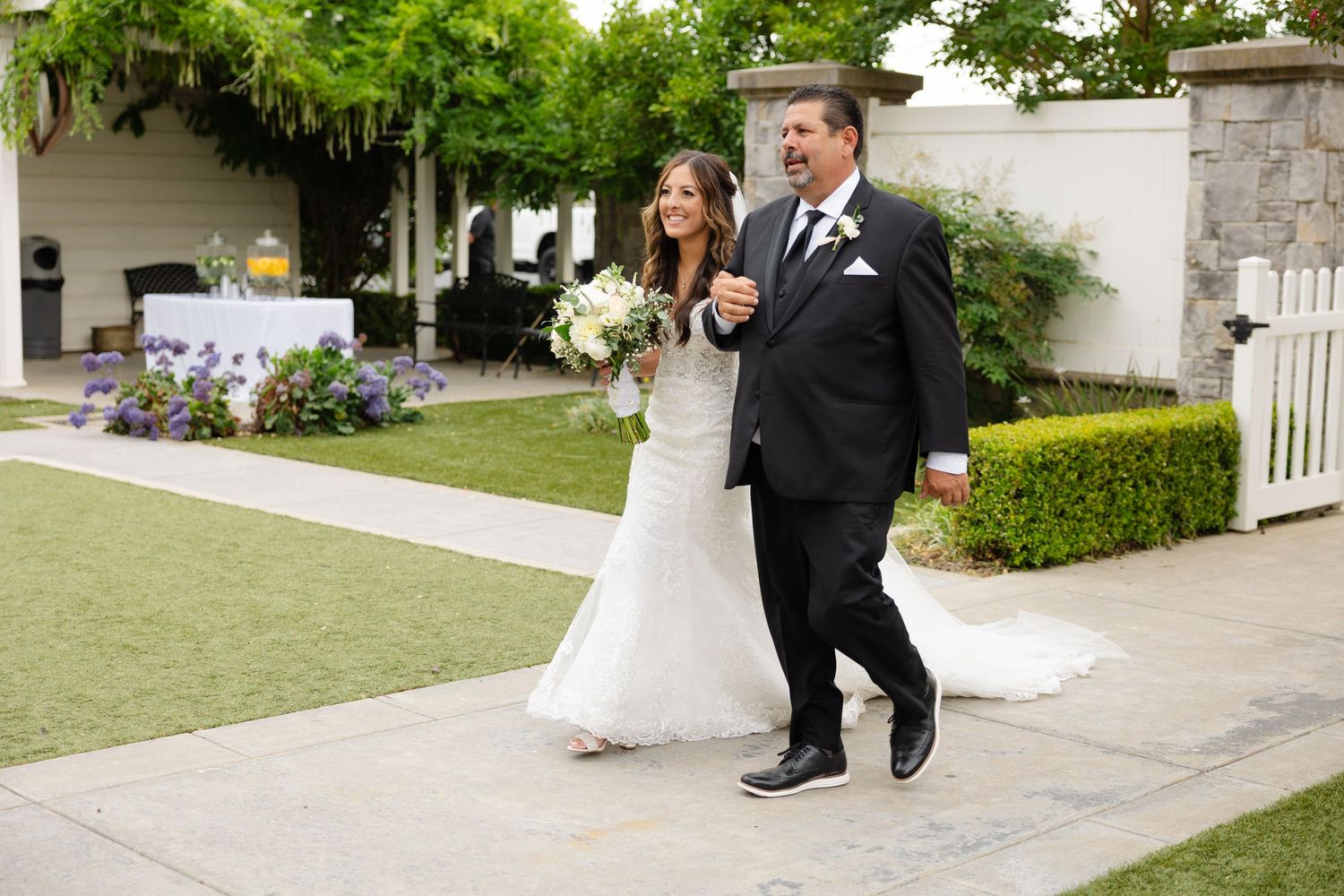A couple walks together during an outdoor wedding ceremony on a manicured lawn with white decorations.