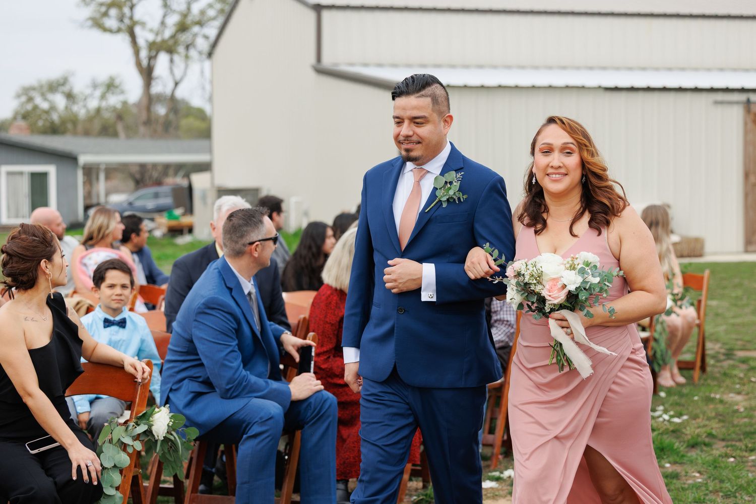 A wedding celebration with people dancing and embracing in a rustic outdoor setting.