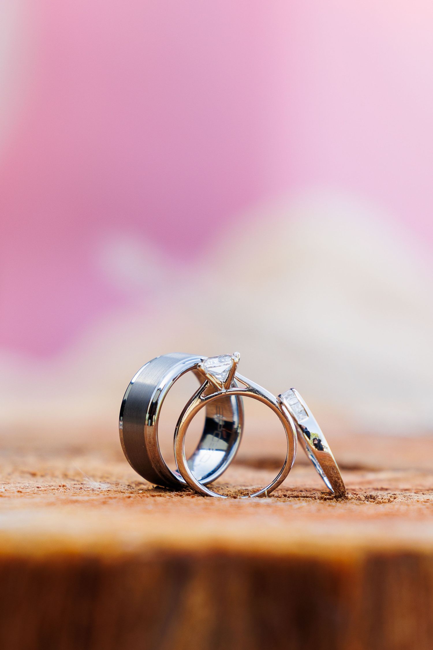 Wedding rings photographed in macro on wooden surface with soft pink background blur.