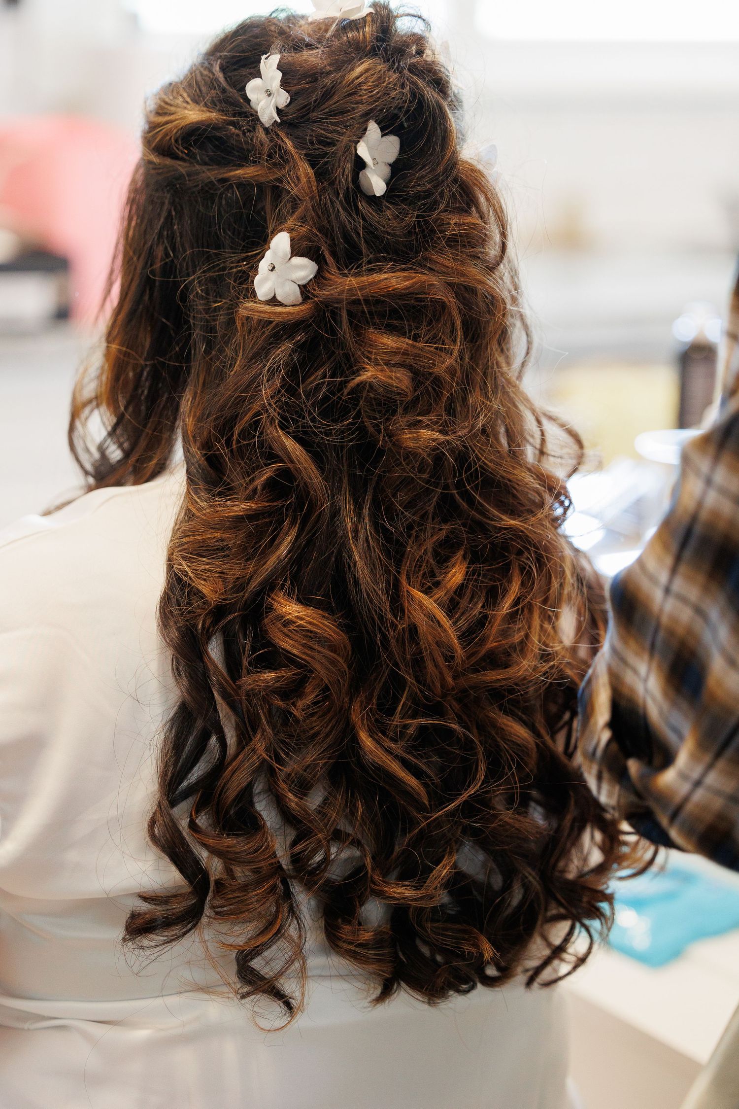 Elegant curled brown hair styled with small white floral accessories for a romantic bridal look.