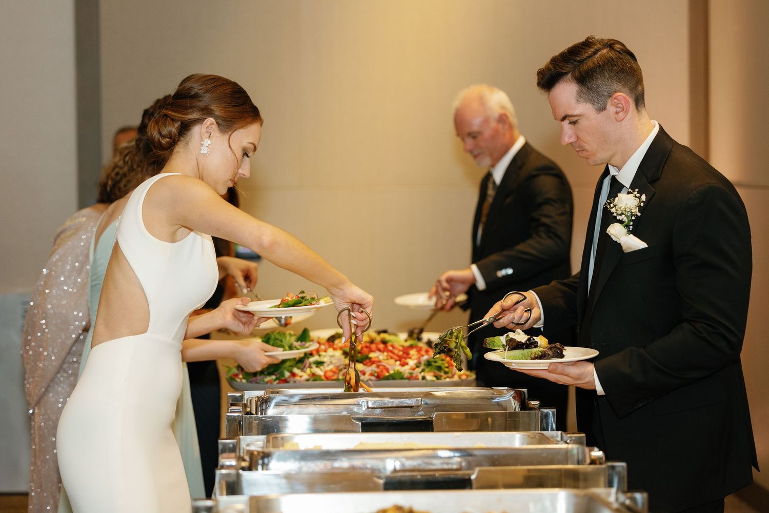 Wedding guests serve themselves from an elegant buffet line with silver chafing dishes at a formal reception.