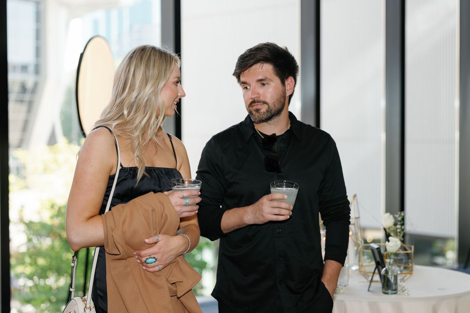 People in formal attire having conversations at a social gathering in a bright modern venue.