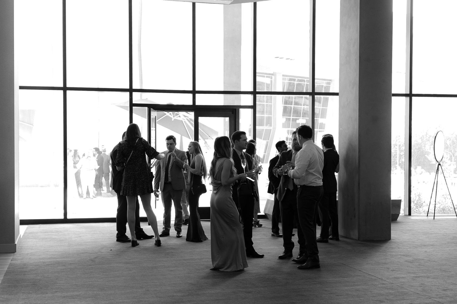 A group of people stand in silhouette against large windows in a modern building interior.