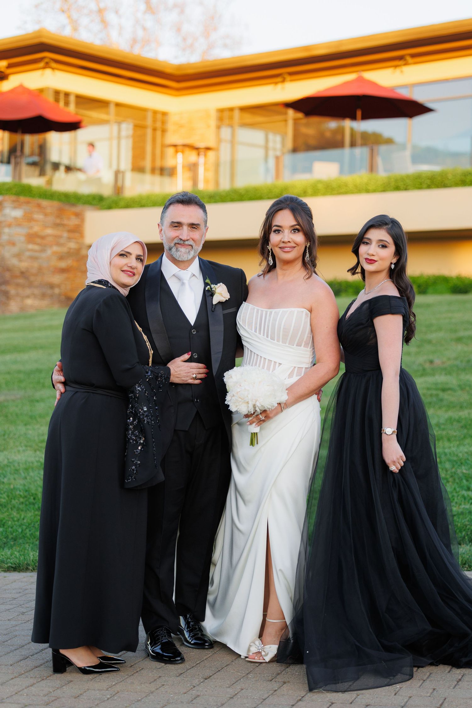 Wedding party wearing black and white formal attire poses together on grassy lawn at outdoor venue.