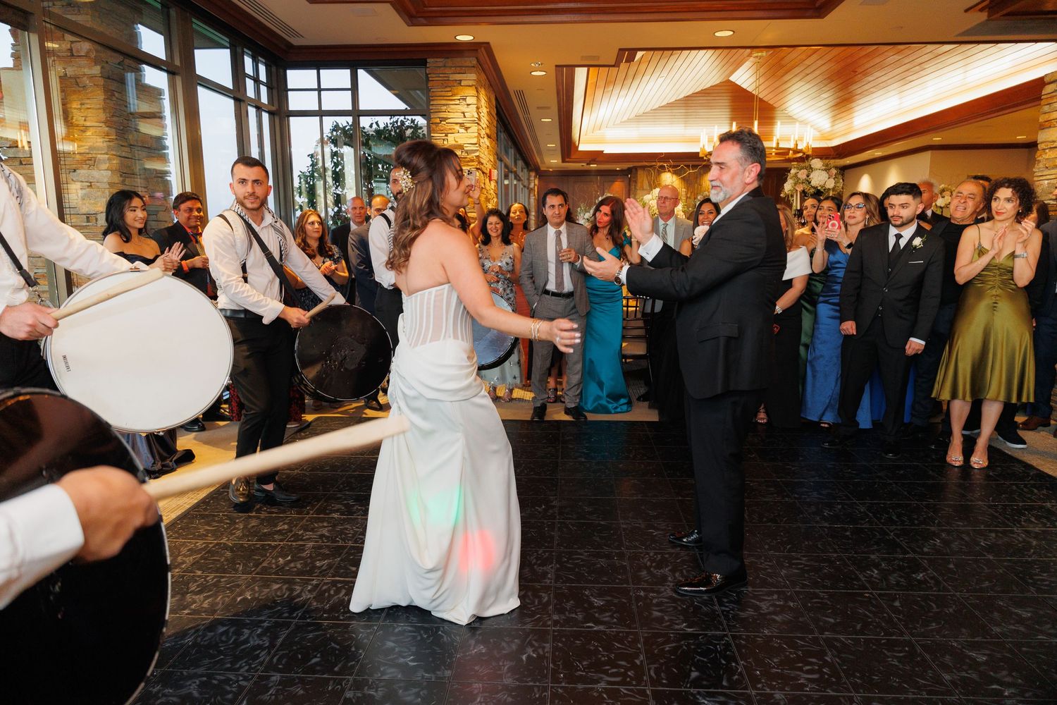 Wedding guests dance and celebrate on a dimly lit dance floor during an evening reception celebration.