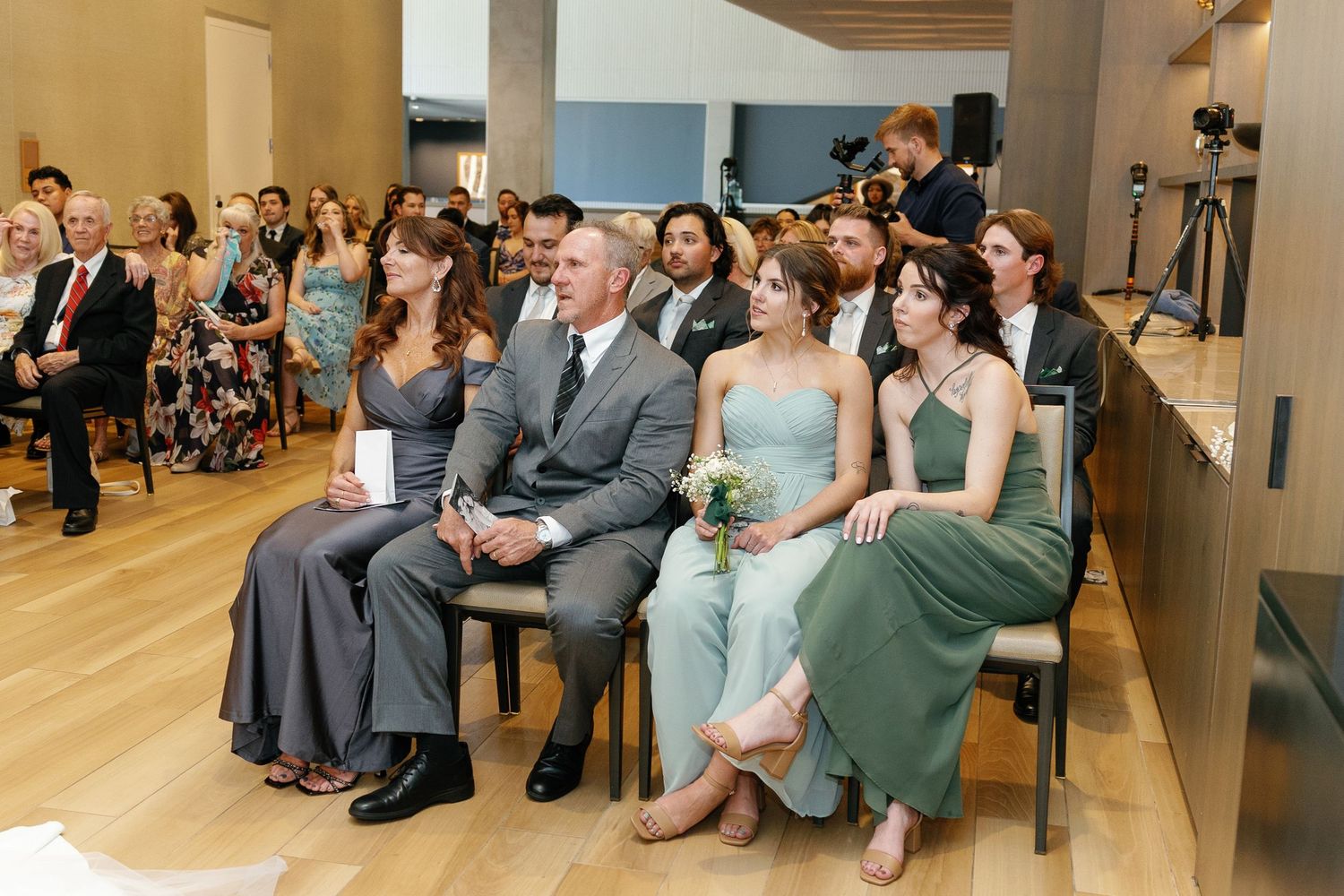 Wedding guests seated in rows during an indoor ceremony with wood floors and modern decor.