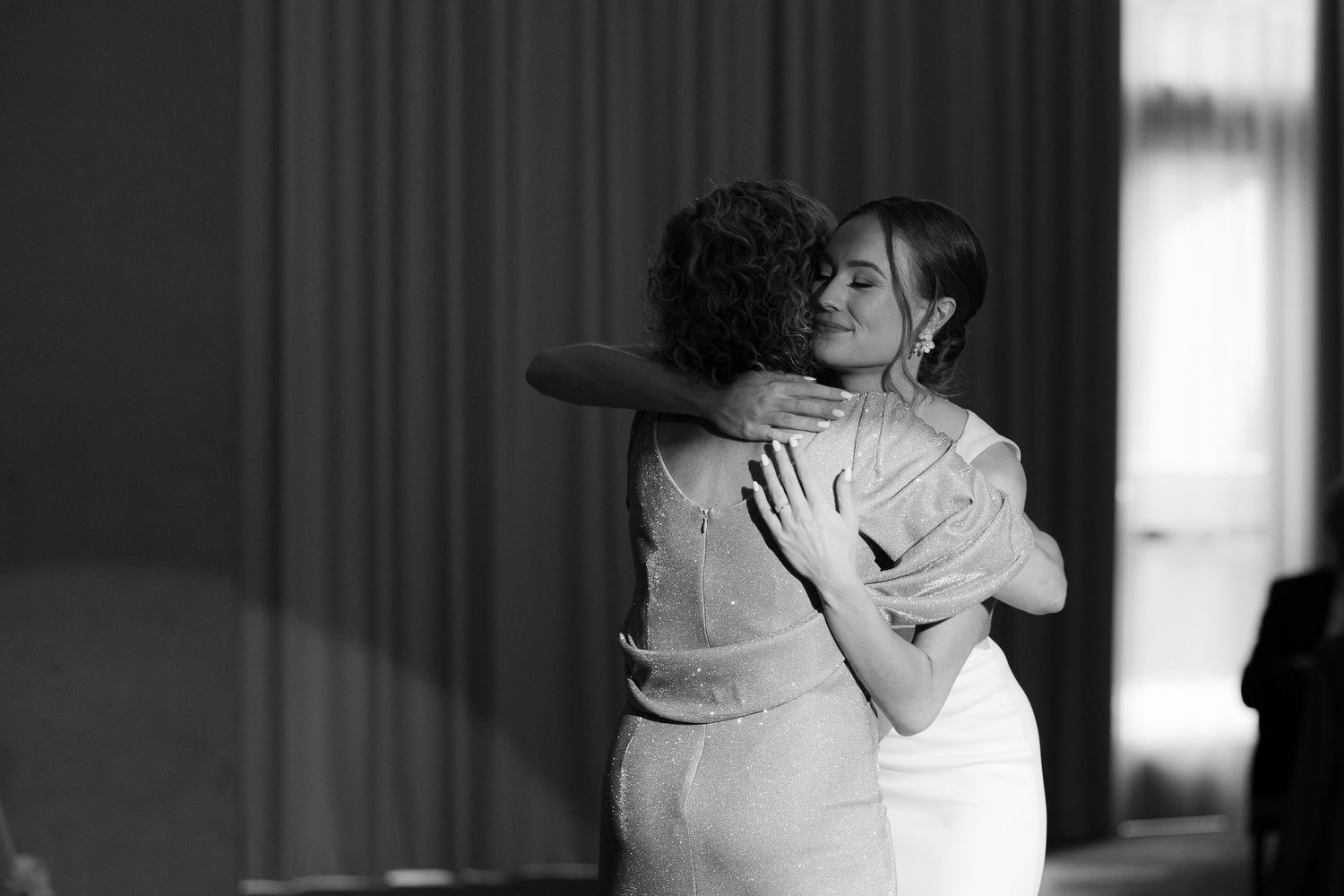 A tender black and white photograph captures two people embracing during a dance in a softly lit room.