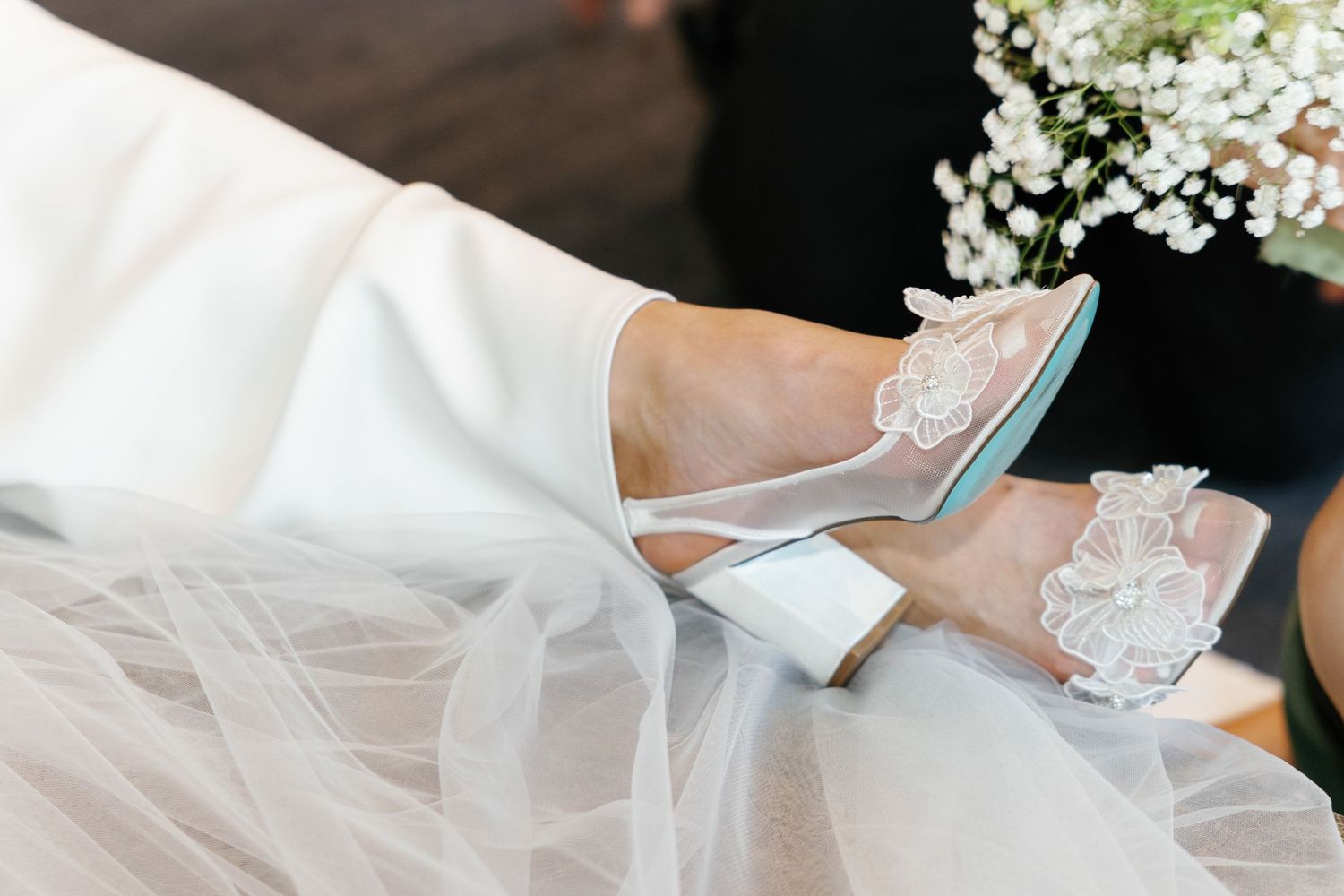 A wedding couple holds hands during their ceremony with white floral decorations and guests in the background.