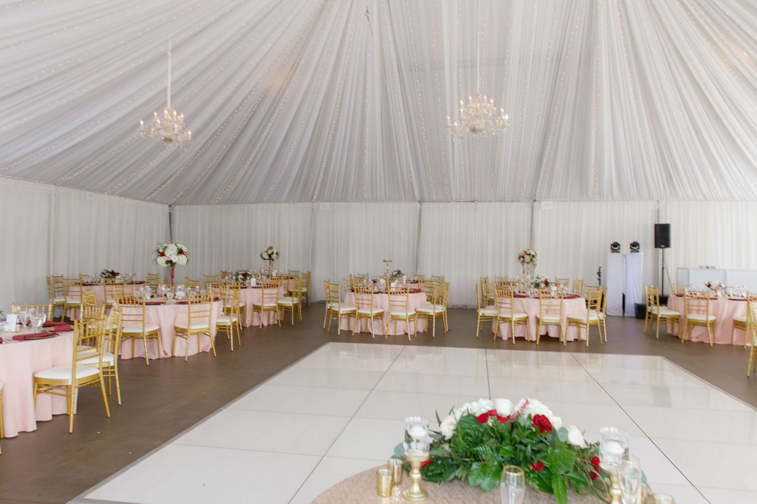 Elegant white wedding reception tent with draped fabric ceiling, crystal chandeliers, and round tables set for dining.