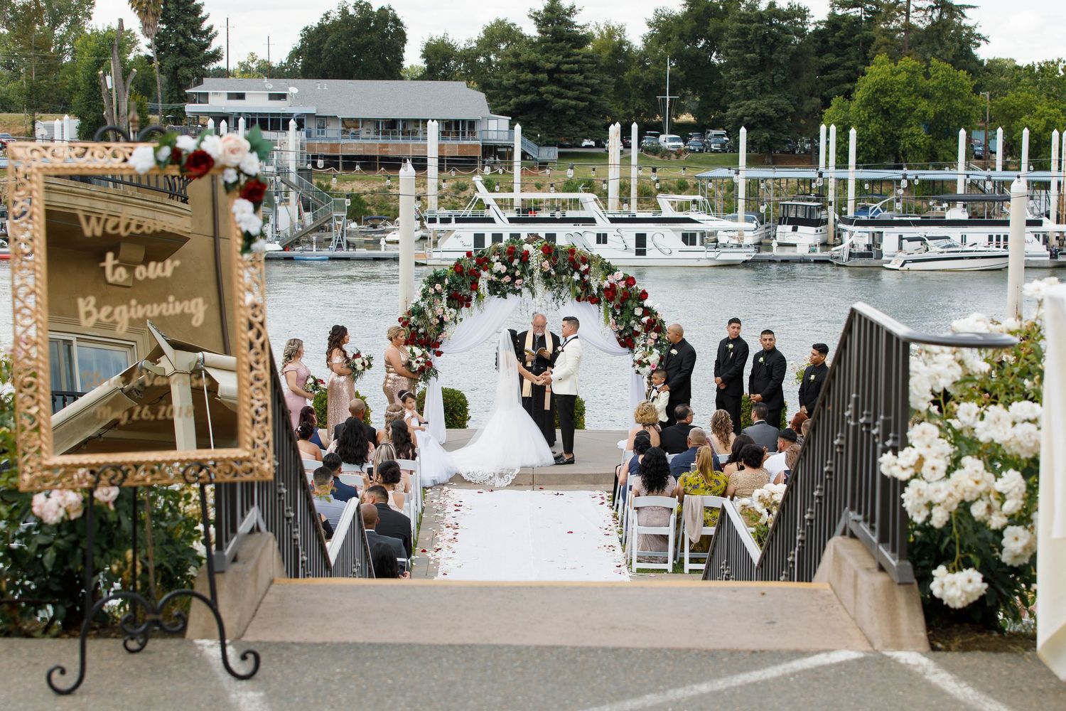 Wedding ceremony setup on a dock with white chairs and floral arrangements overlooking a marina with boats.