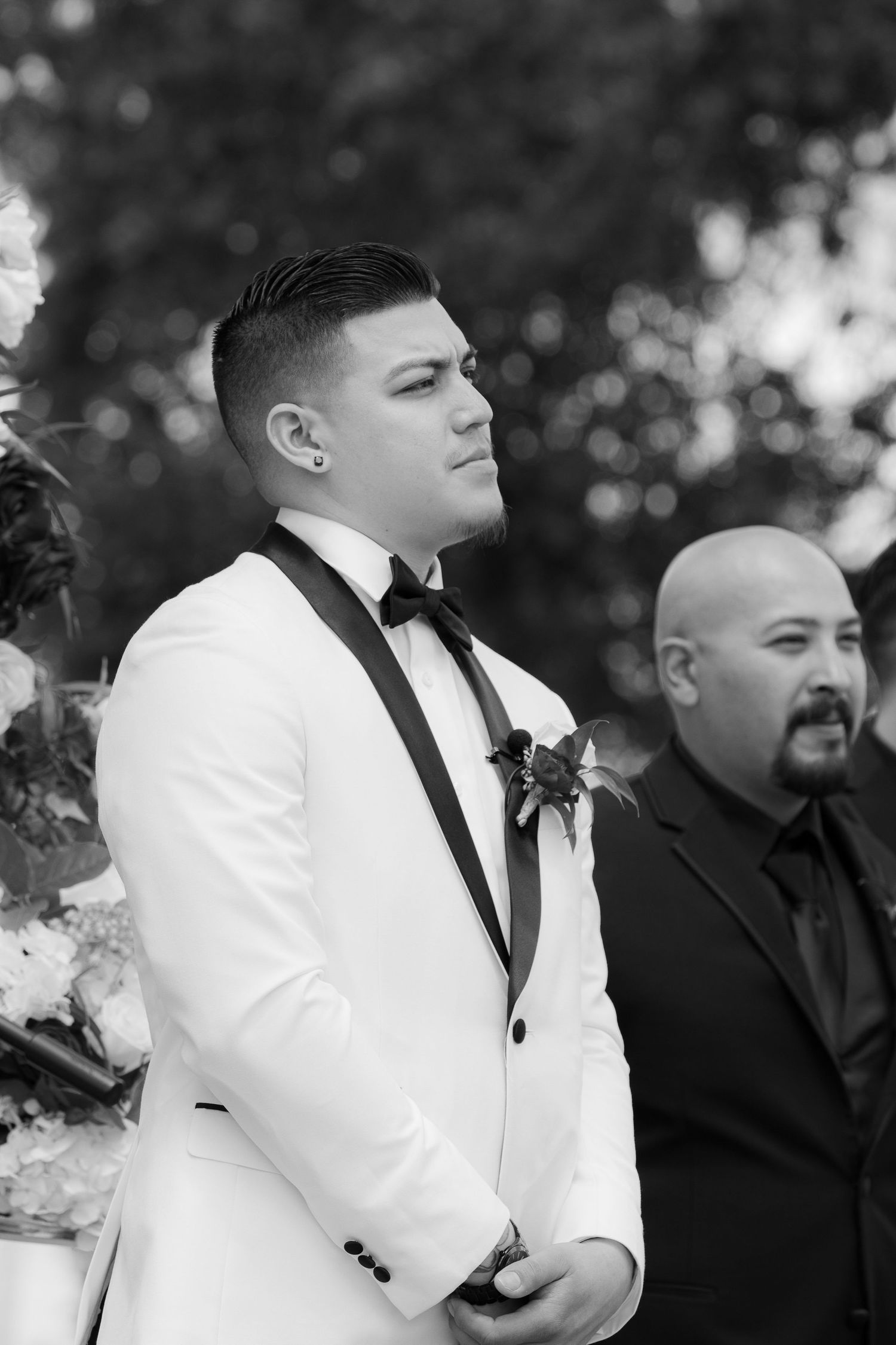 Black and white wedding photo series showing groomsmen in white tuxedo jacket and black tie standing with others in formal wear.
