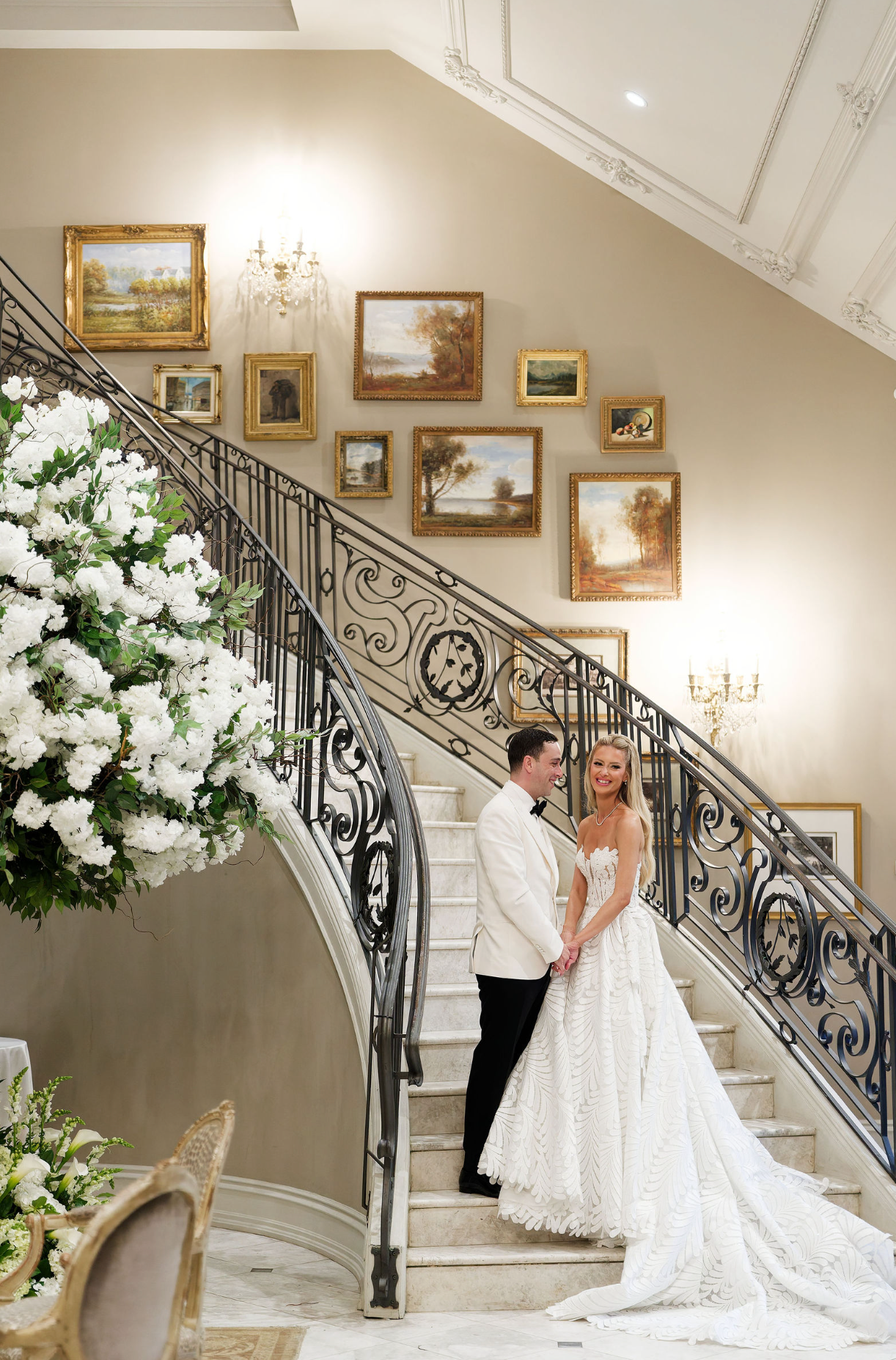 Elegant wedding venue staircase with ornate iron railings and white floral arrangements showcases romantic bridal portraits.