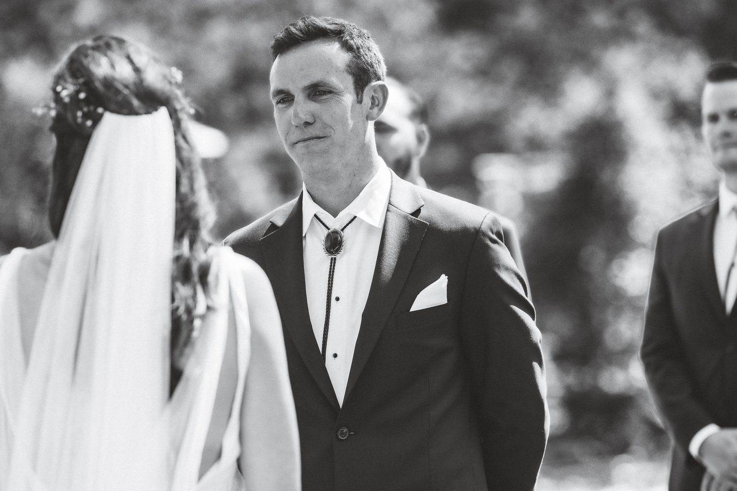 Black and white photo of a wedding ceremony showing a groom in a suit looking lovingly at his bride in her veil.