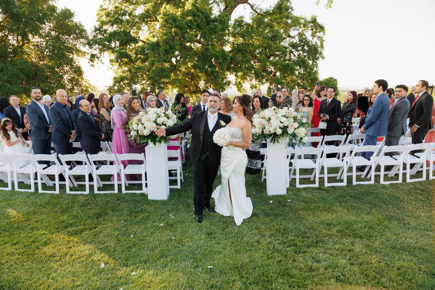 Elegant outdoor wedding ceremony venue with rows of white folding chairs set up on a green lawn at sunset.