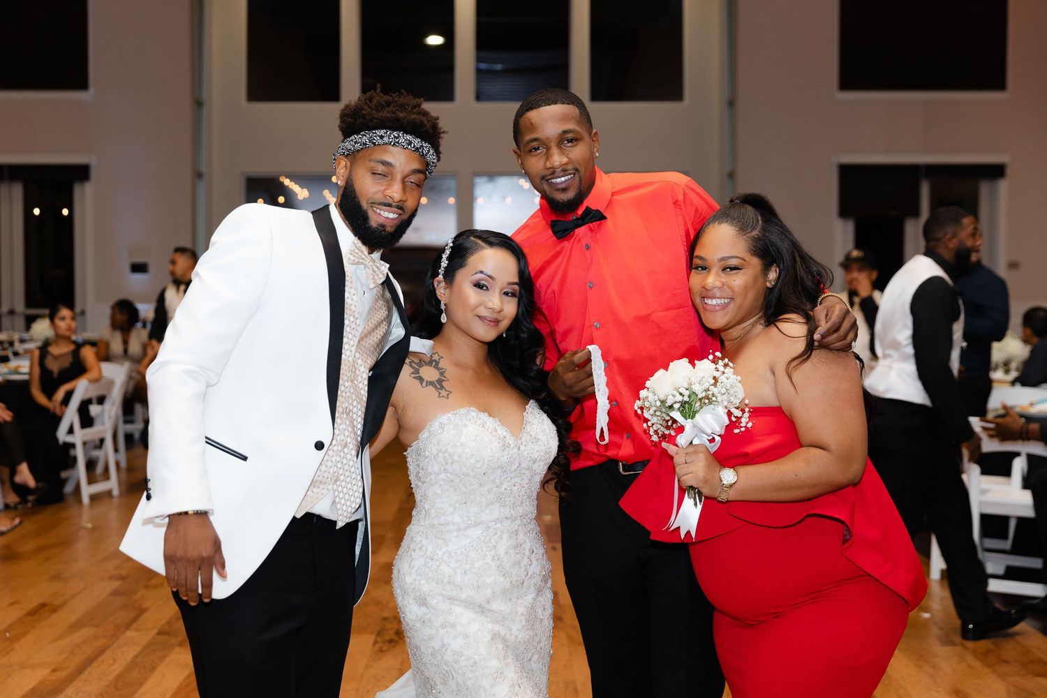 Wedding celebration with bride in white dress and guests in formal attire posing together at indoor reception venue.