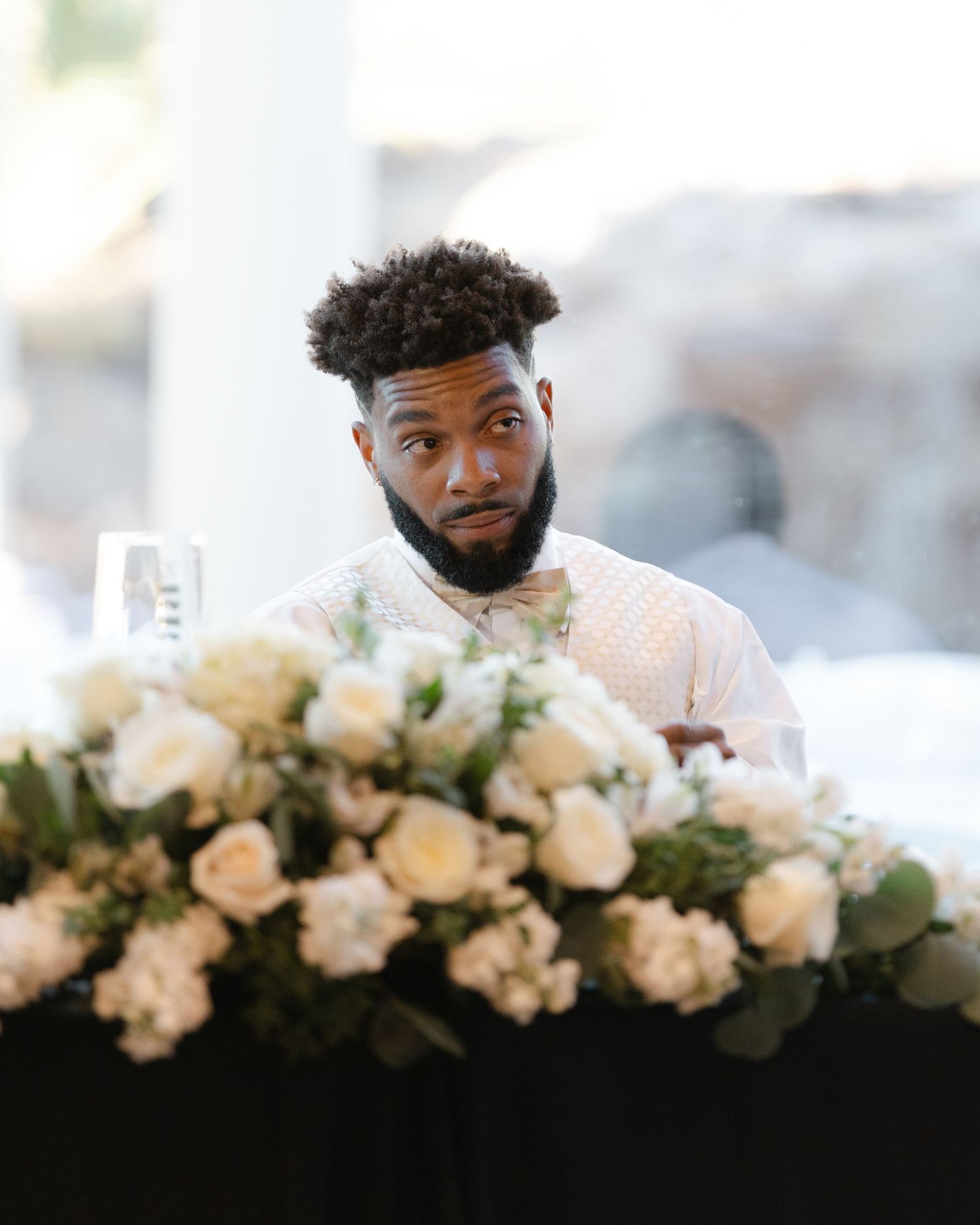 A row of white roses and greenery decorates the edge of a dark surface in an elegant display.