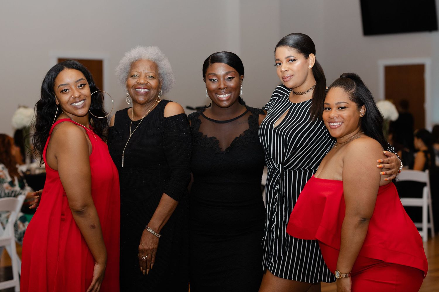 A group of friends pose together at a social event wearing red and black outfits.
