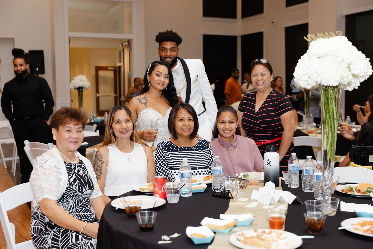People seated at long tables during a dinner event with white floral centerpieces and place settings.