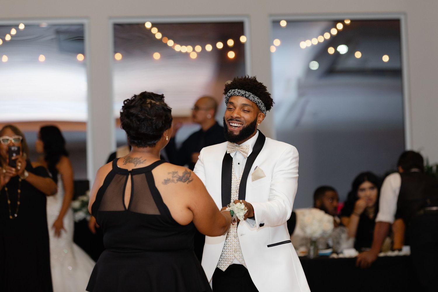Wedding guests dance and celebrate on a dimly lit dance floor with string lights glowing overhead during a reception.
