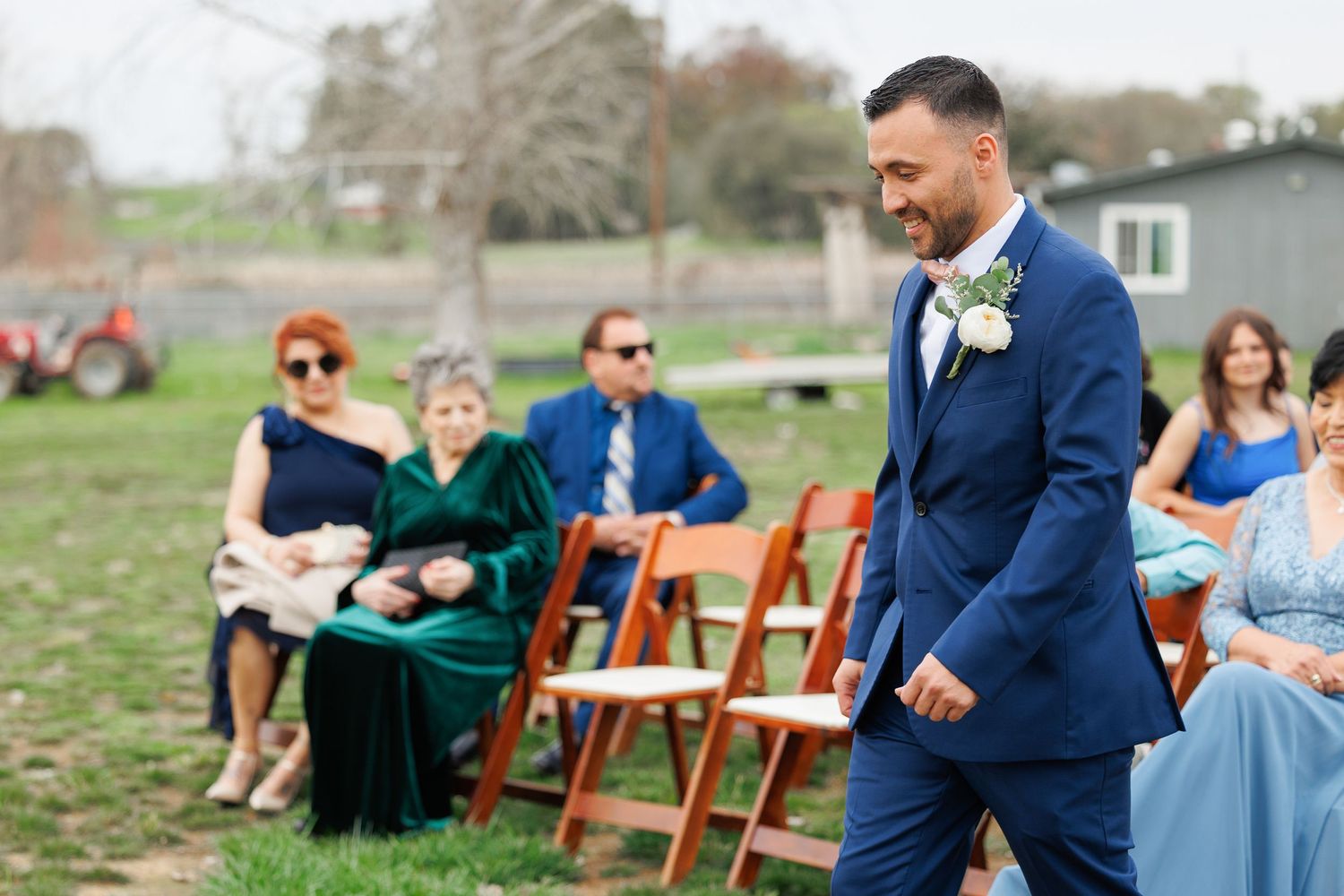 A wedding party laughs together during an outdoor ceremony with wooden chairs and green grass in the background.