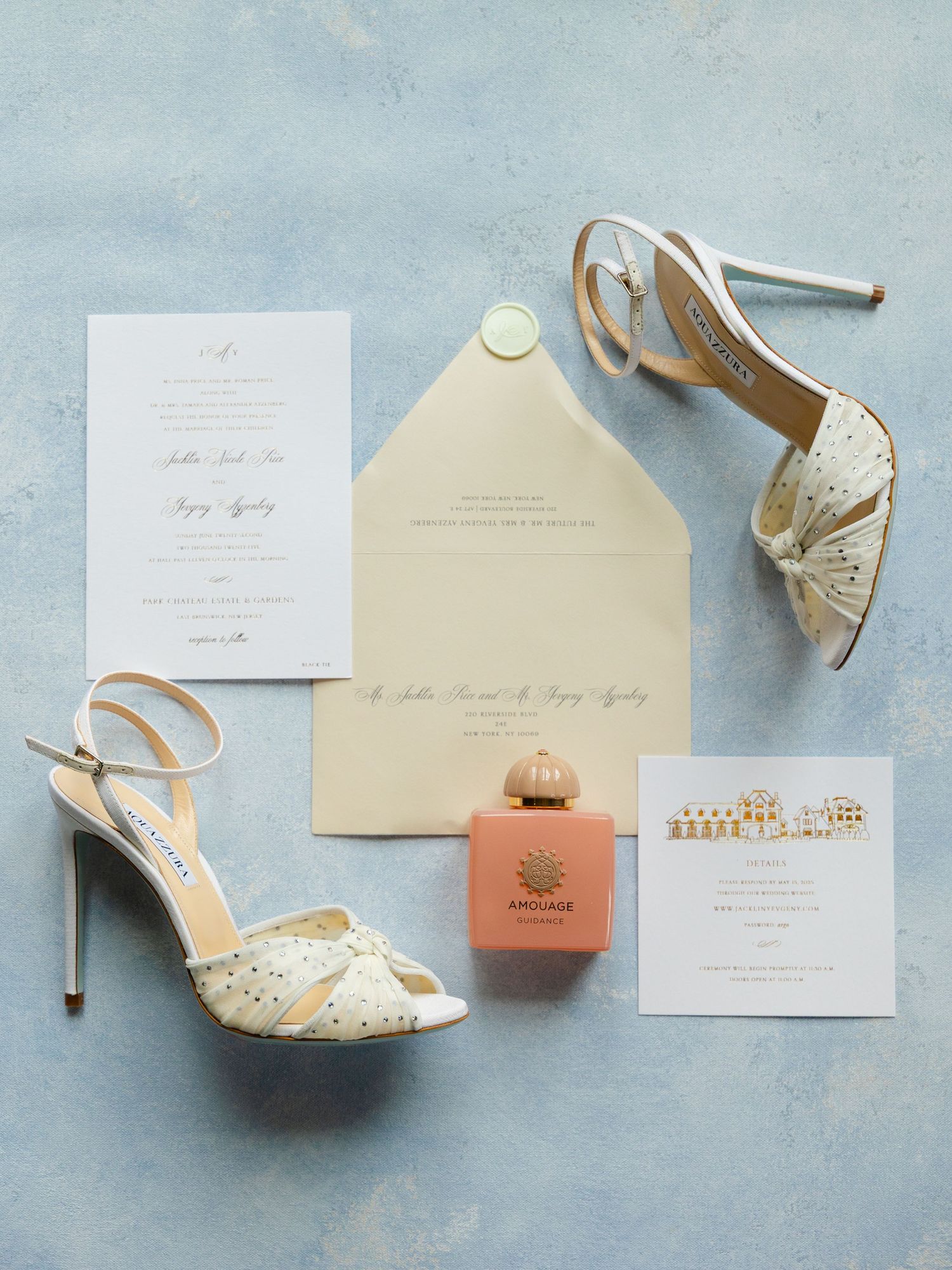 Elegant wedding flat lay with glittery heels, Amouage perfume, cream envelope, and gold-detailed invitations on blue backdrop.