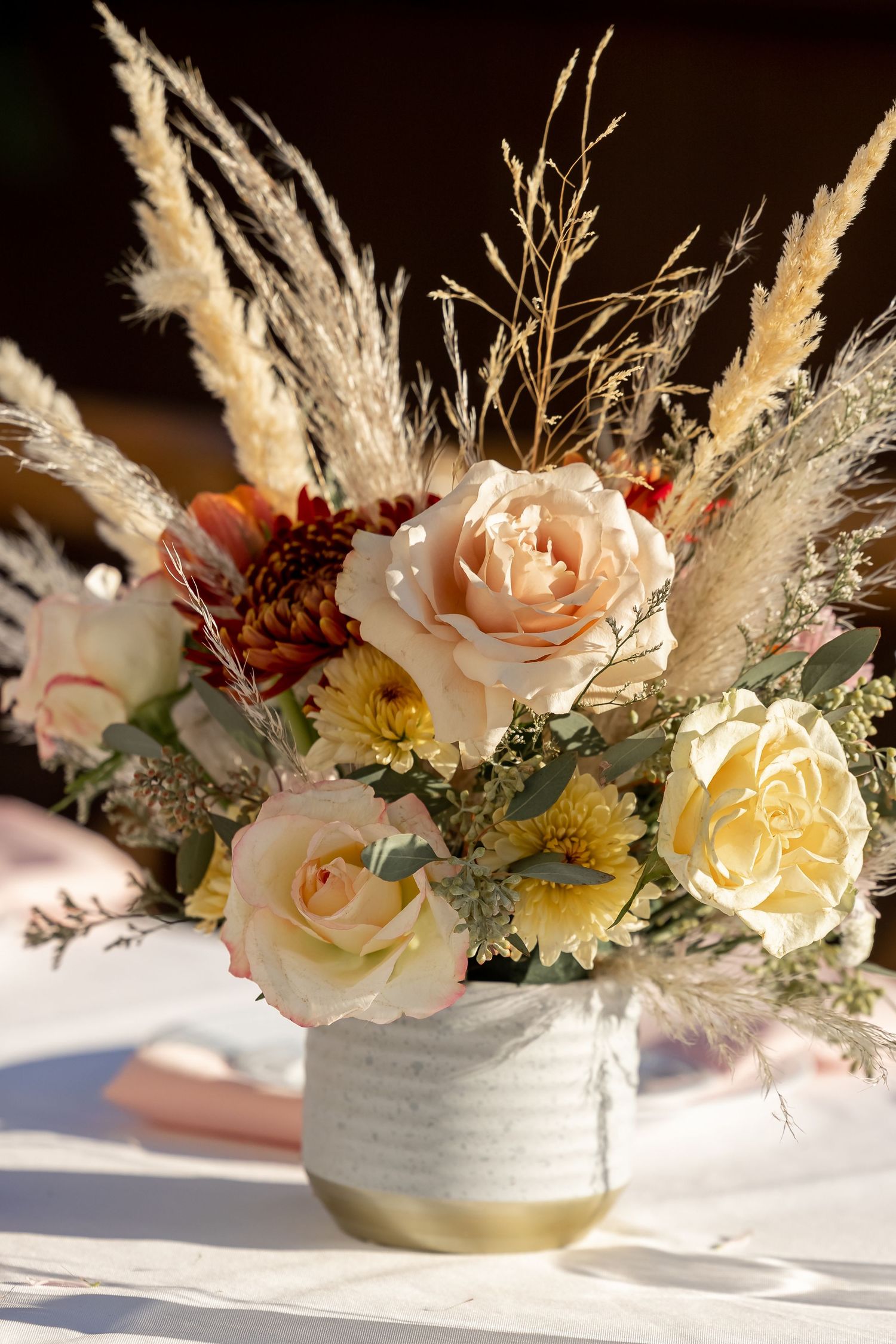 Elegant floral centerpiece featuring pale peach roses, dried pampas grass, and yellow flowers in a white ceramic bowl.