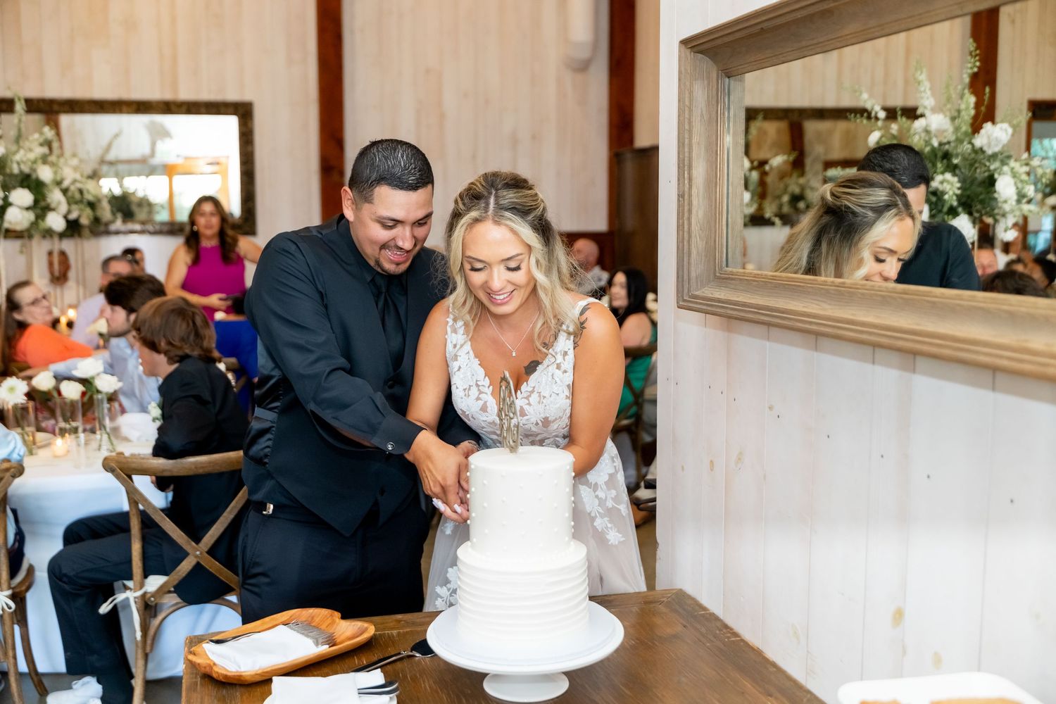 A wedding reception scene with elegant table settings and white floral arrangements.