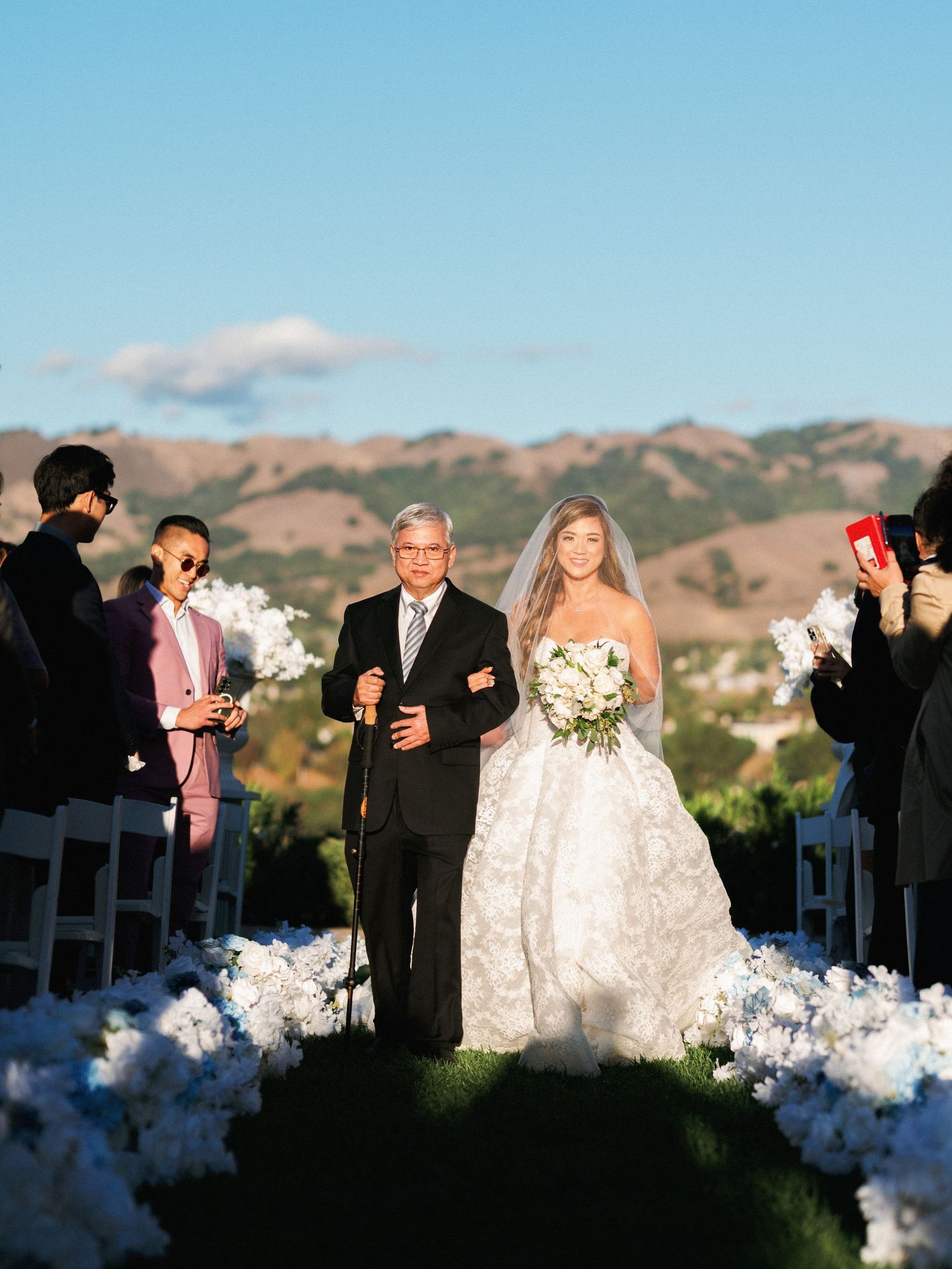 Wedding ceremony processional with mountain backdrop and white floral aisle decorations at sunset.